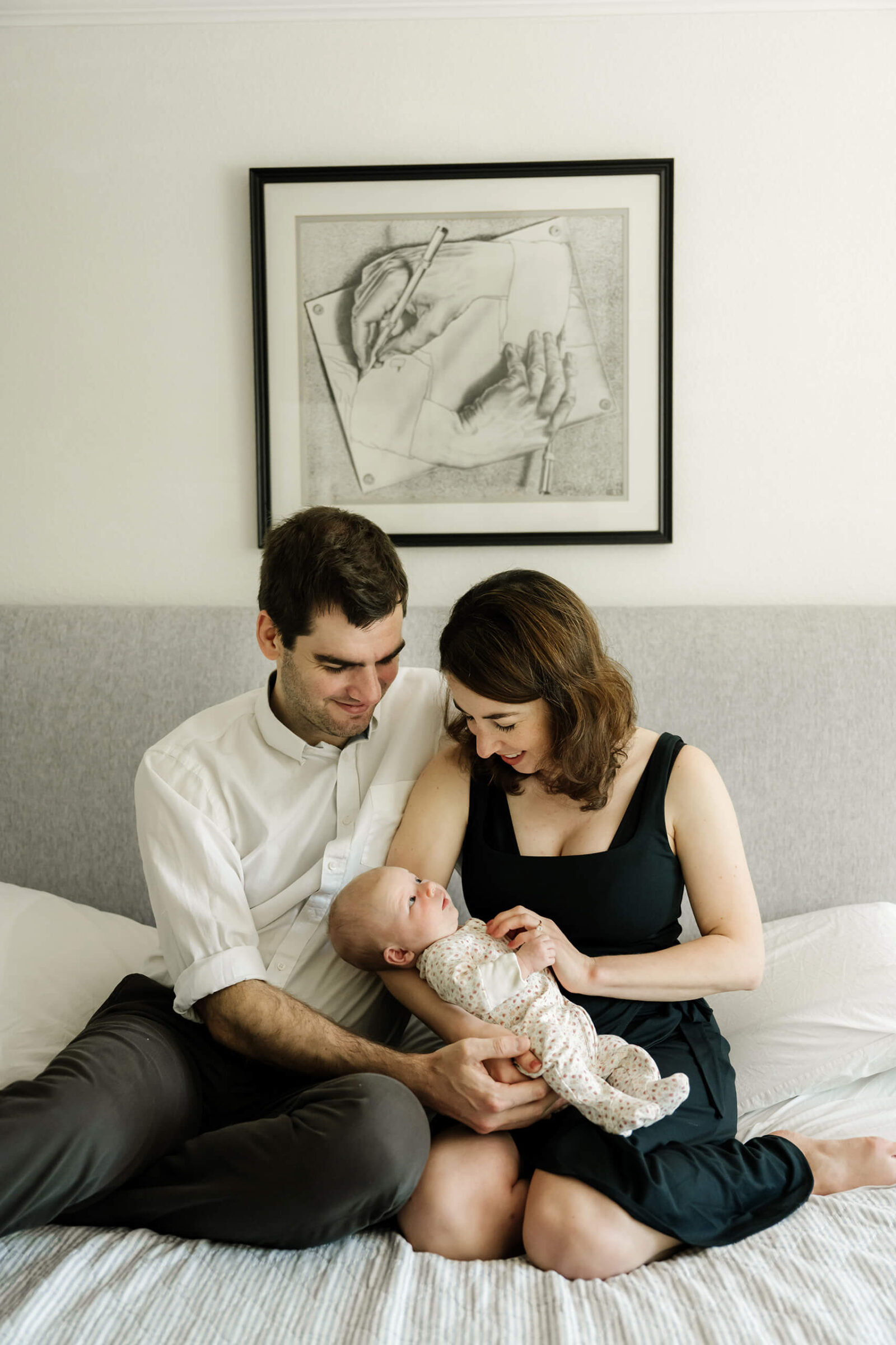 Family sitting on their bed smiling at their baby during a relaxed, heartfelt in-home newborn photo session in Seattle.