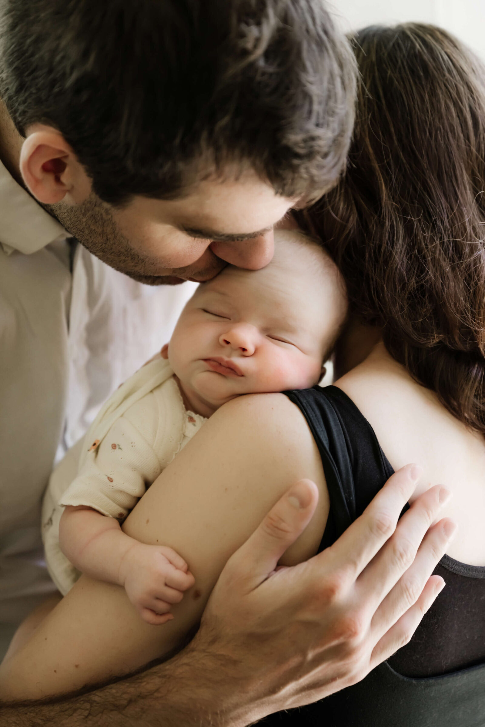 Father kissing newborn’s head as mother holds the baby close during a tender and natural lifestyle newborn photoshoot.