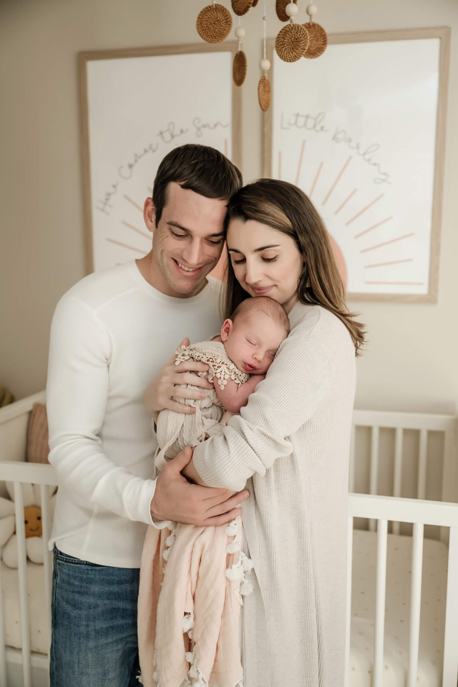 Parents embracing their sleeping newborn in a softly lit nursery during a calm and connection-centered in-home newborn photoshoot.