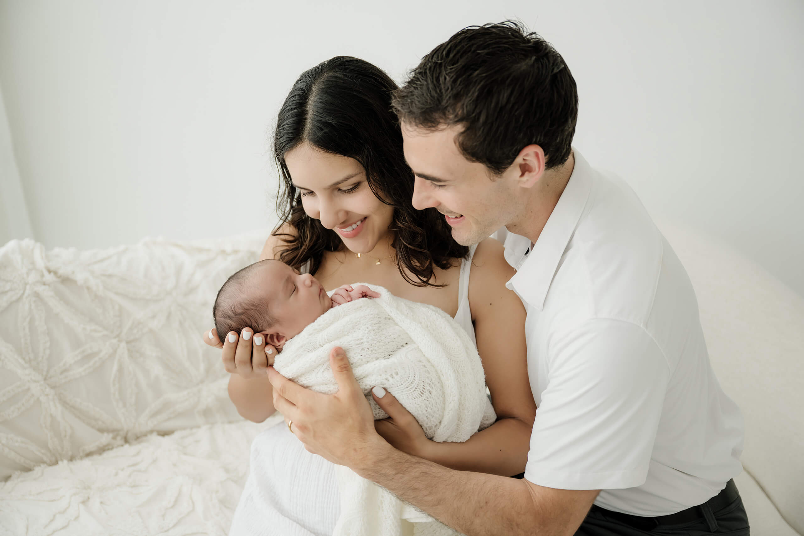 Parents smiling at their baby wrapped in a white blanket during a gentle newborn photoshoot in Seattle area studio.
