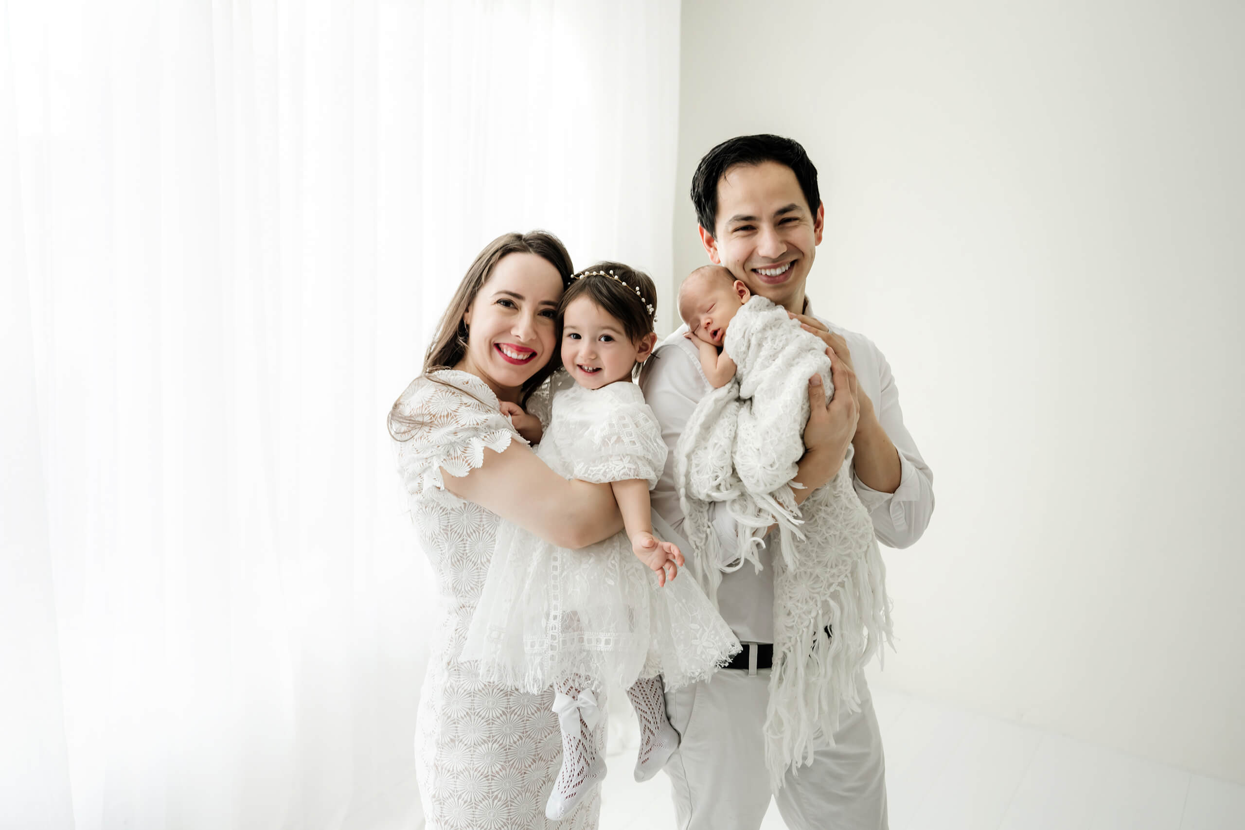 Family with toddler and newborn baby in soft white tones during a natural light newborn photoshoot in Seattle.