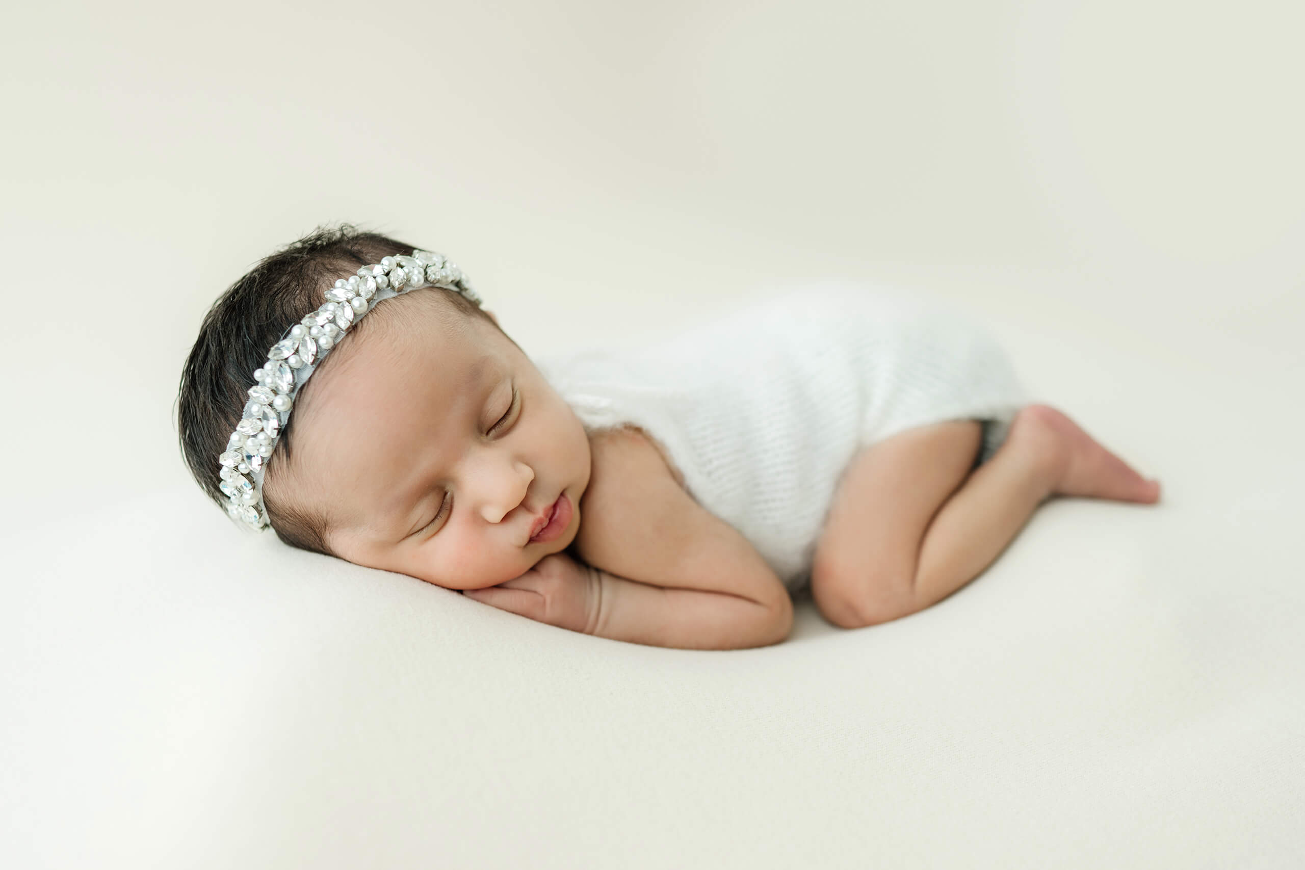 Close-up of a sleeping newborn in a white knitted wrap during a professional photo session for newborn.