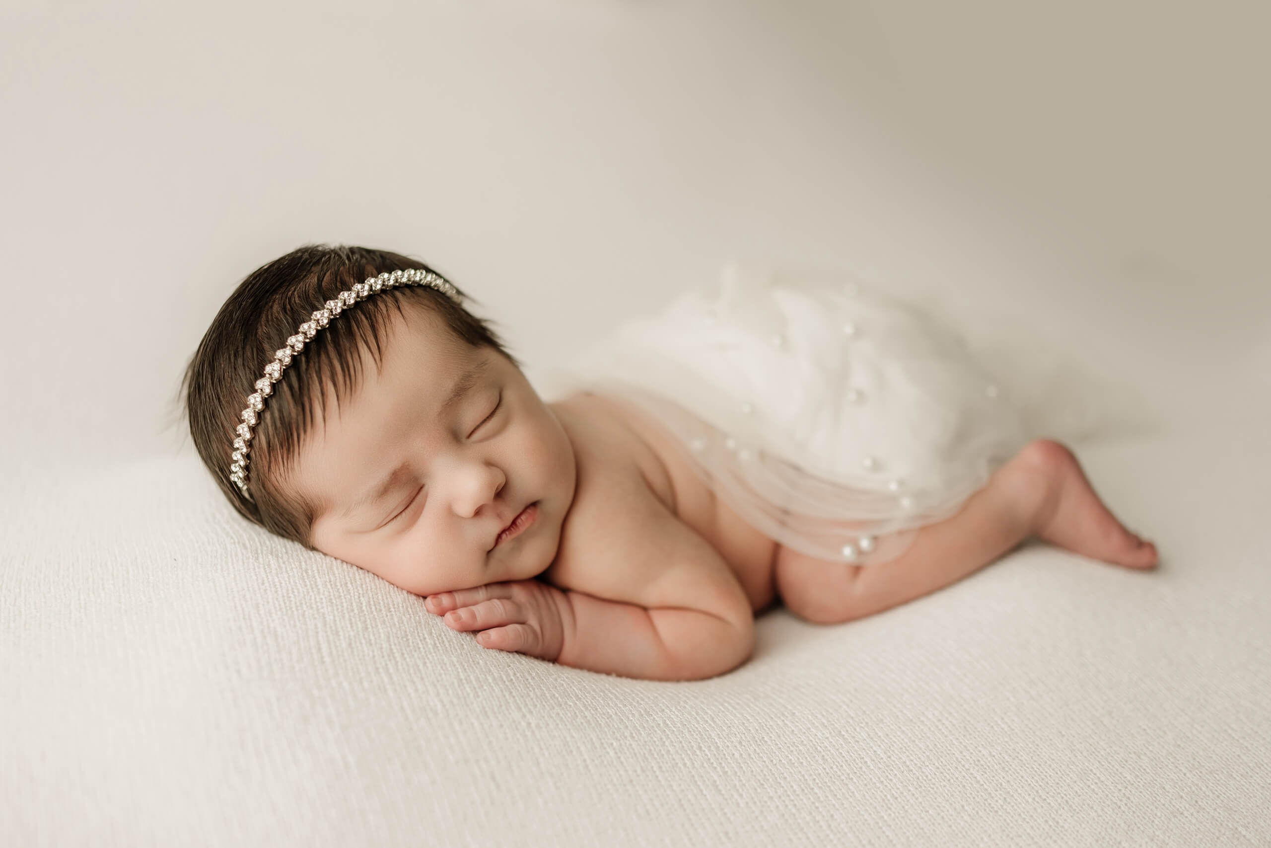 Sleeping newborn baby wearing a pearl headband during a light-filled Seattle newborn photoshoot.