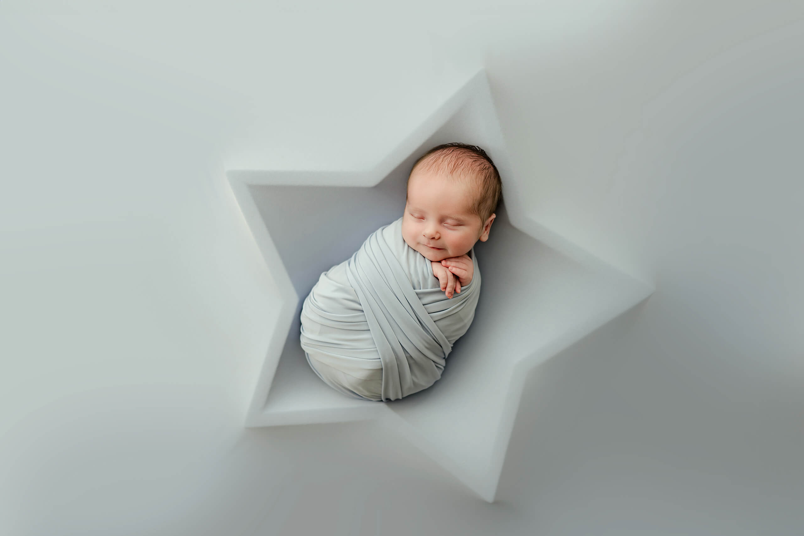 Wrapped baby sleeping in a star-shaped prop during a creative, minimalist newborn photoshoot in Kirkland studio.