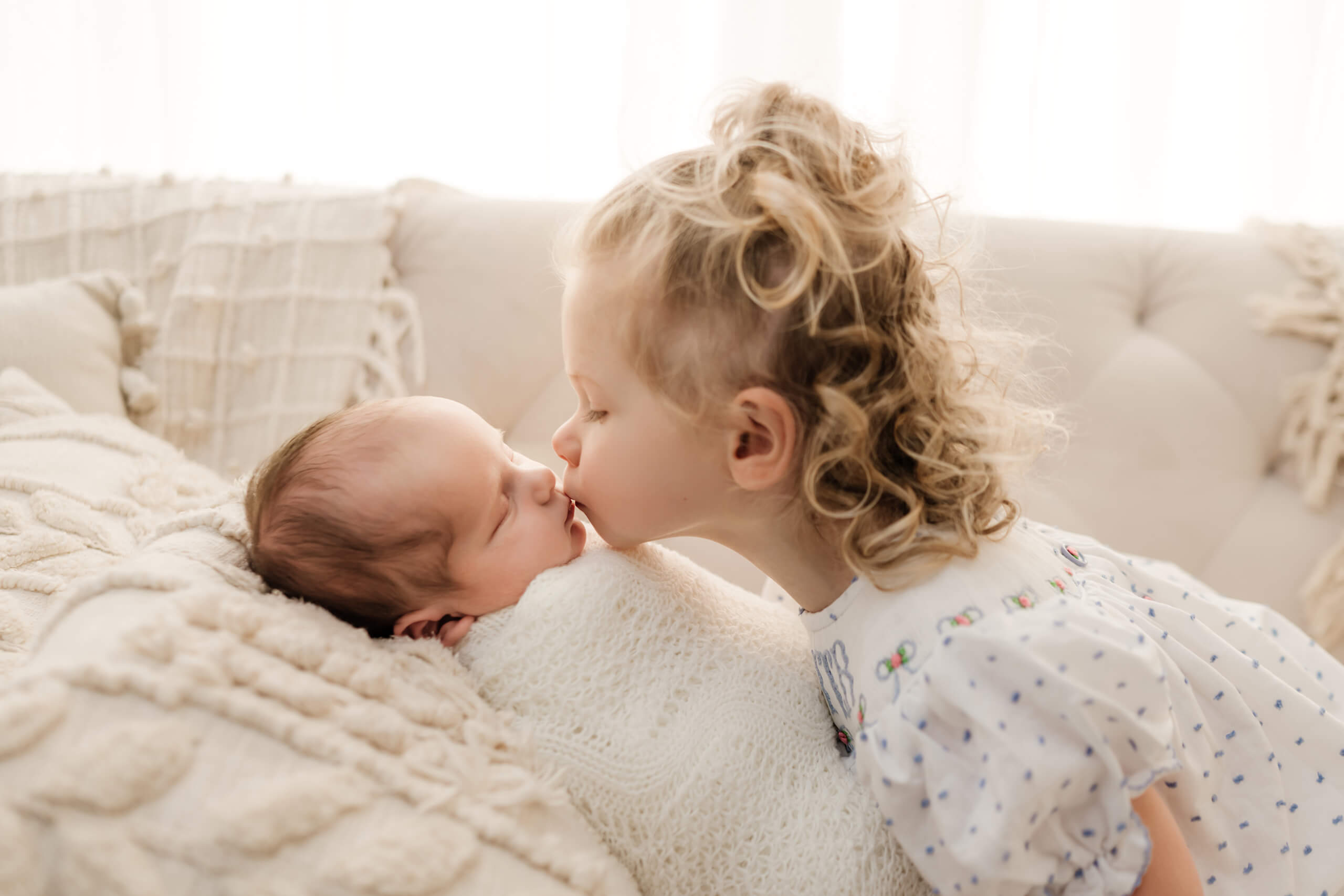Big sister kissing her newborn baby brother during a light-filled newborn photoshoot in Seattle studio.
