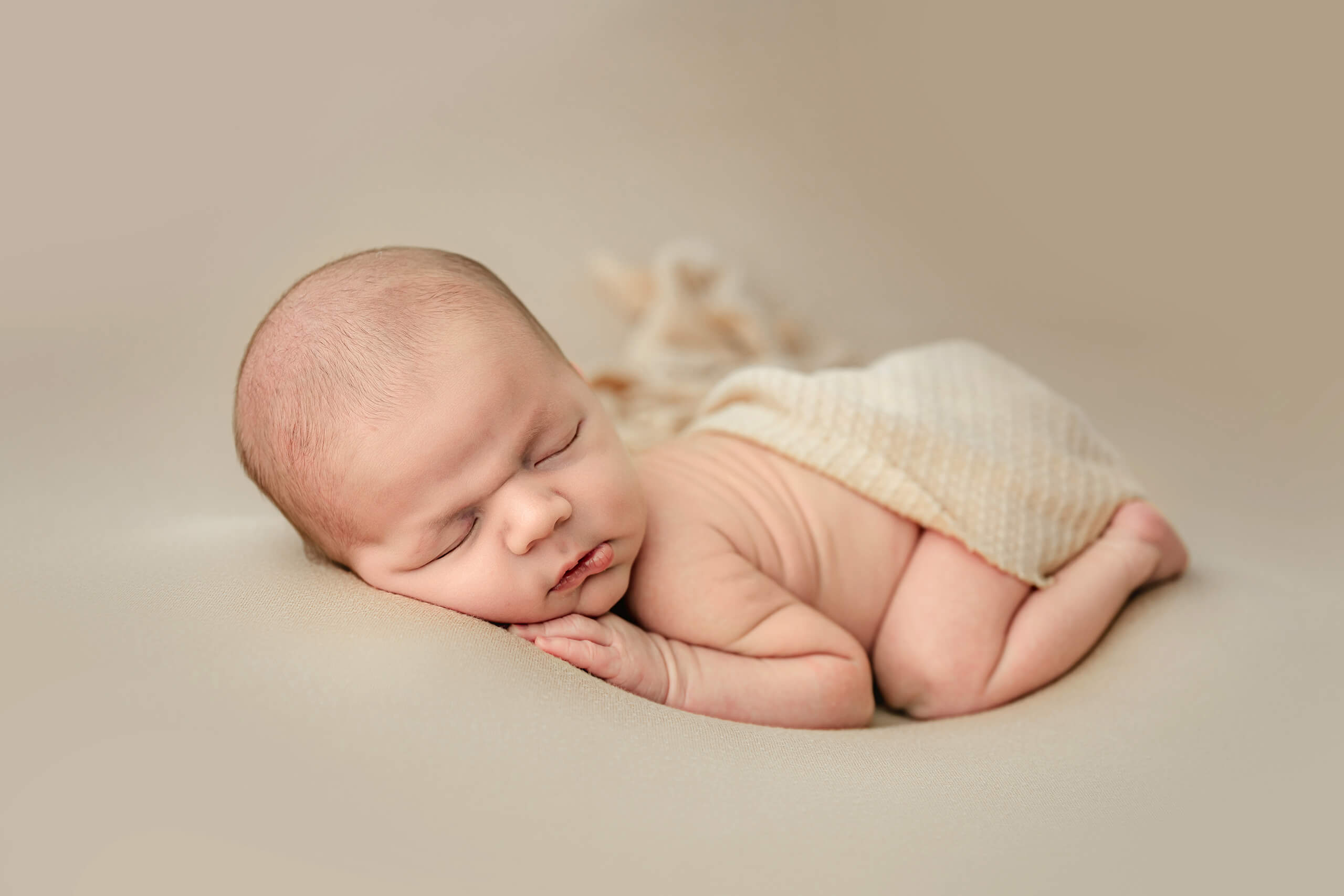 Sleeping baby on beige background during a minimalist, natural newborn photoshoot in Kirkland studio.
