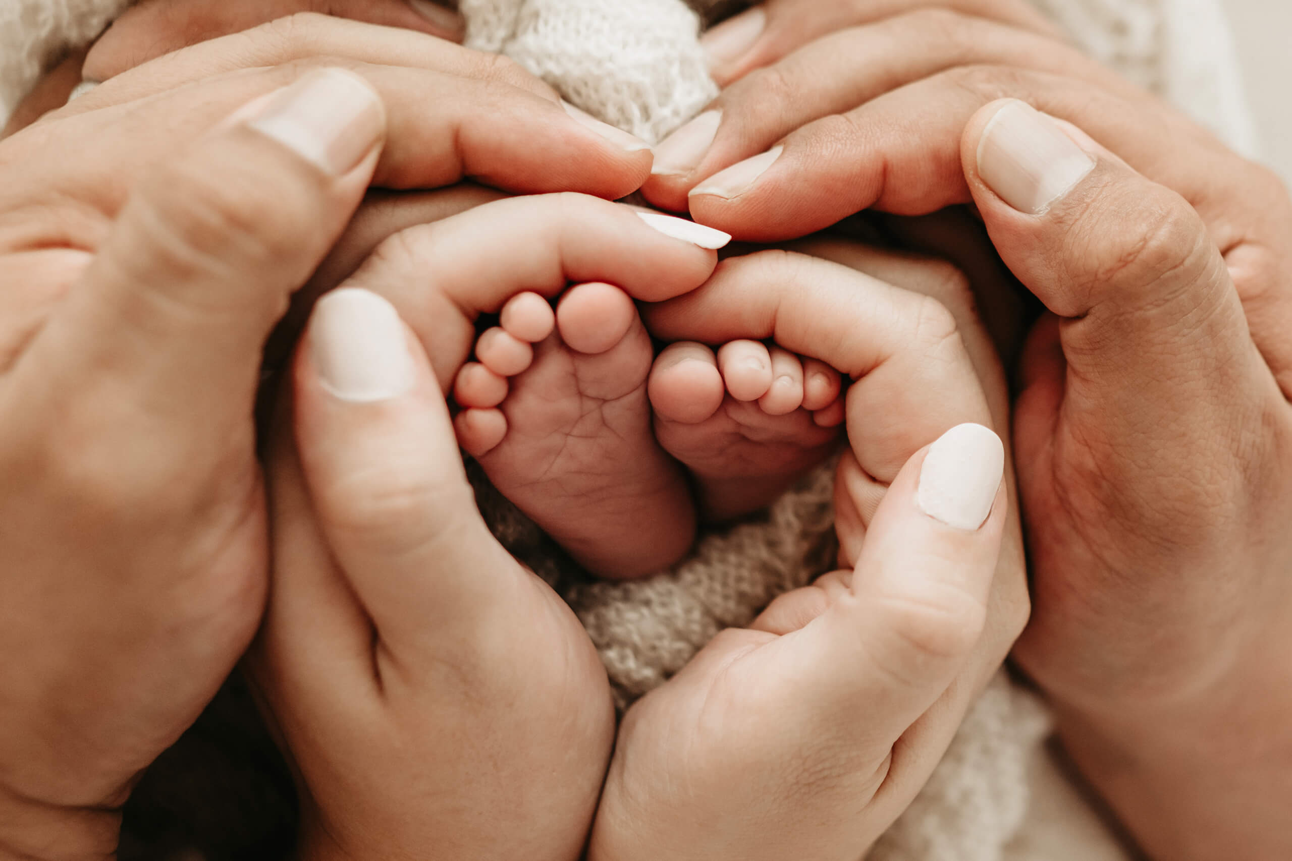 Parents&rsquo; hands forming a heart around their baby&rsquo;s tiny feet during a professional photo session for newborn.