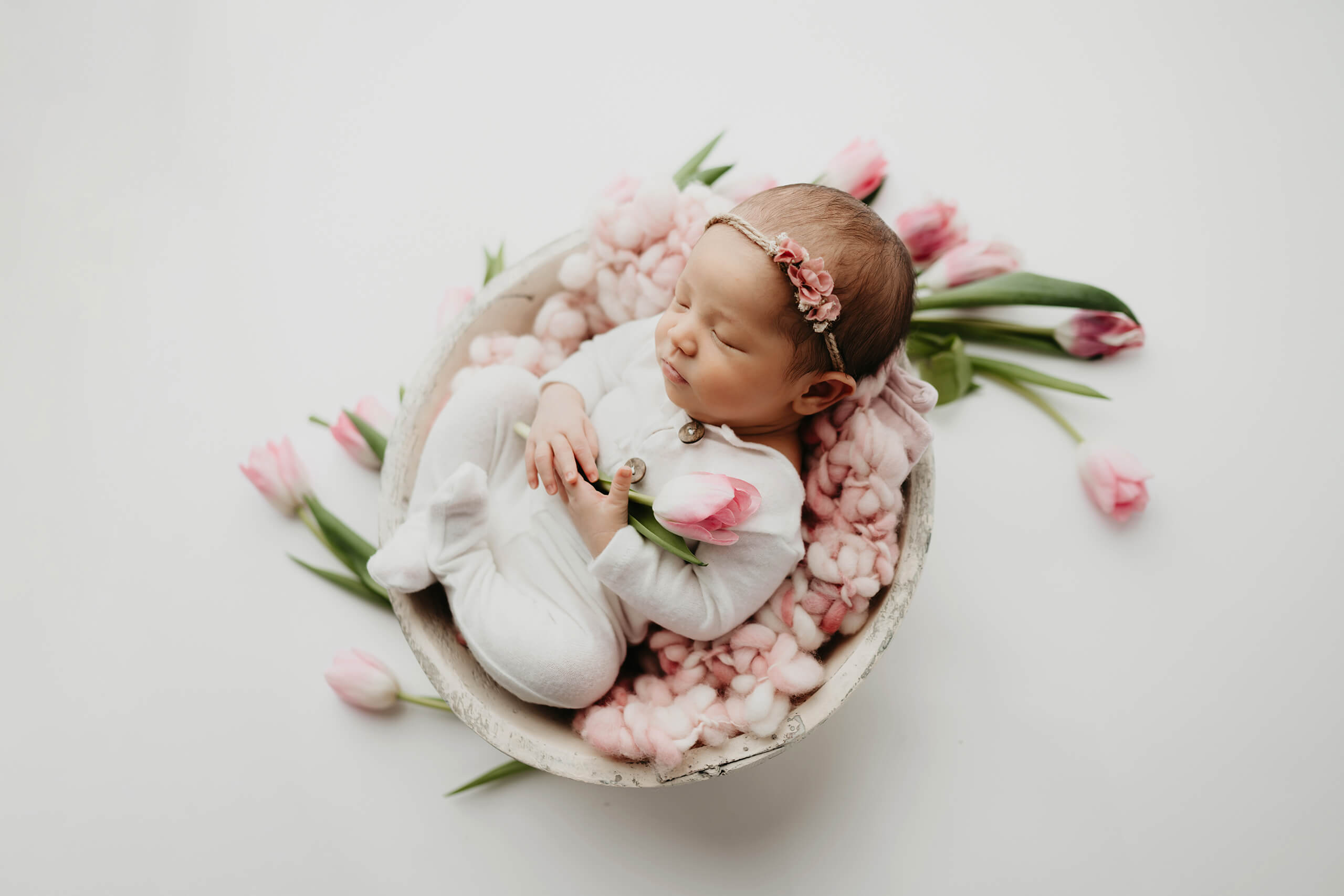 Newborn baby sleeping in a white bowl surrounded by pink tulips during a floral-themed Seattle newborn photoshoot.