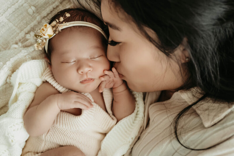 Mother kissing her newborn baby’s cheek during a soft, light-filled newborn session in Seattle studio.