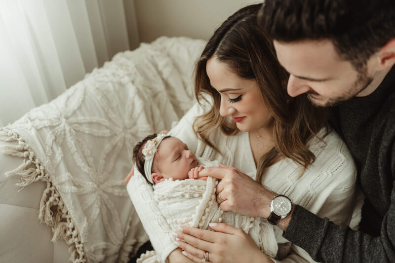 Mother and father admiring their sleeping newborn baby wrapped in cream during a cozy studio newborn photoshoot in Seattle.