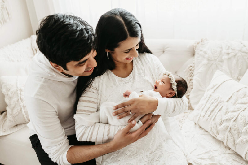 Parents smiling at their newborn baby wrapped in white during a light-filled studio newborn session in Seattle.