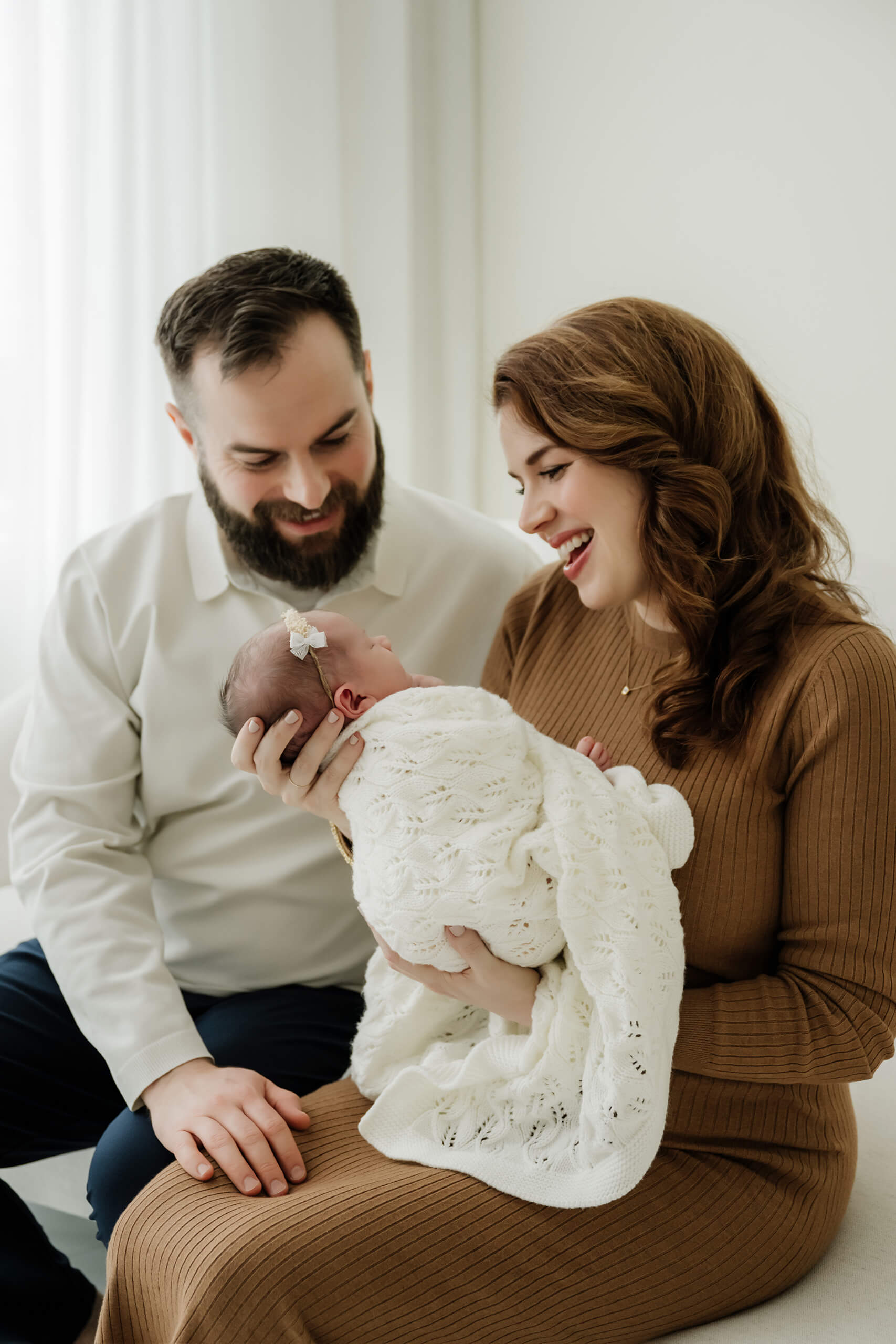 Mom and dad admire their newborn girl in a soft white wrap for a Seattle newborn family photography session in studio