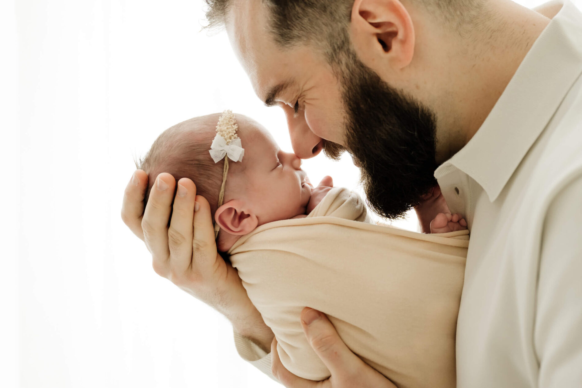 Dad cuddles newborn nose-to-nose in a wrapped pose during a Seattle newborn family photoshoot on a bright white backdrop