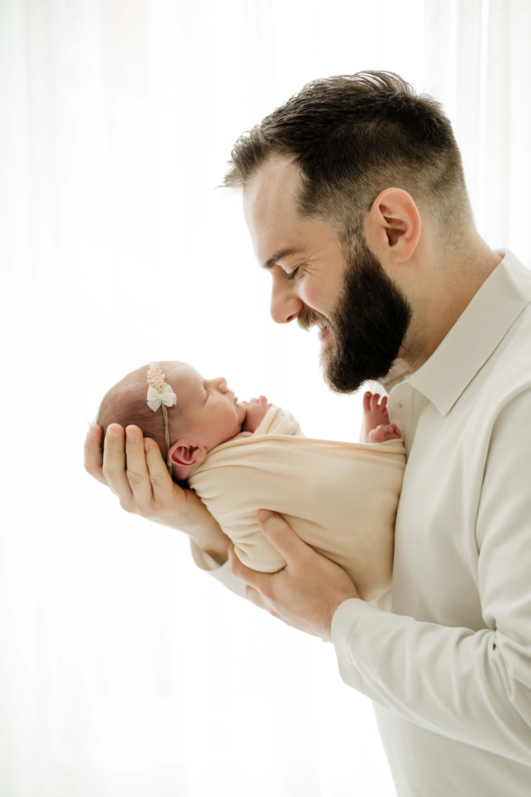 Dad holds a swaddled newborn and smiles during a Seattle family newborn photography session, simple white studio background