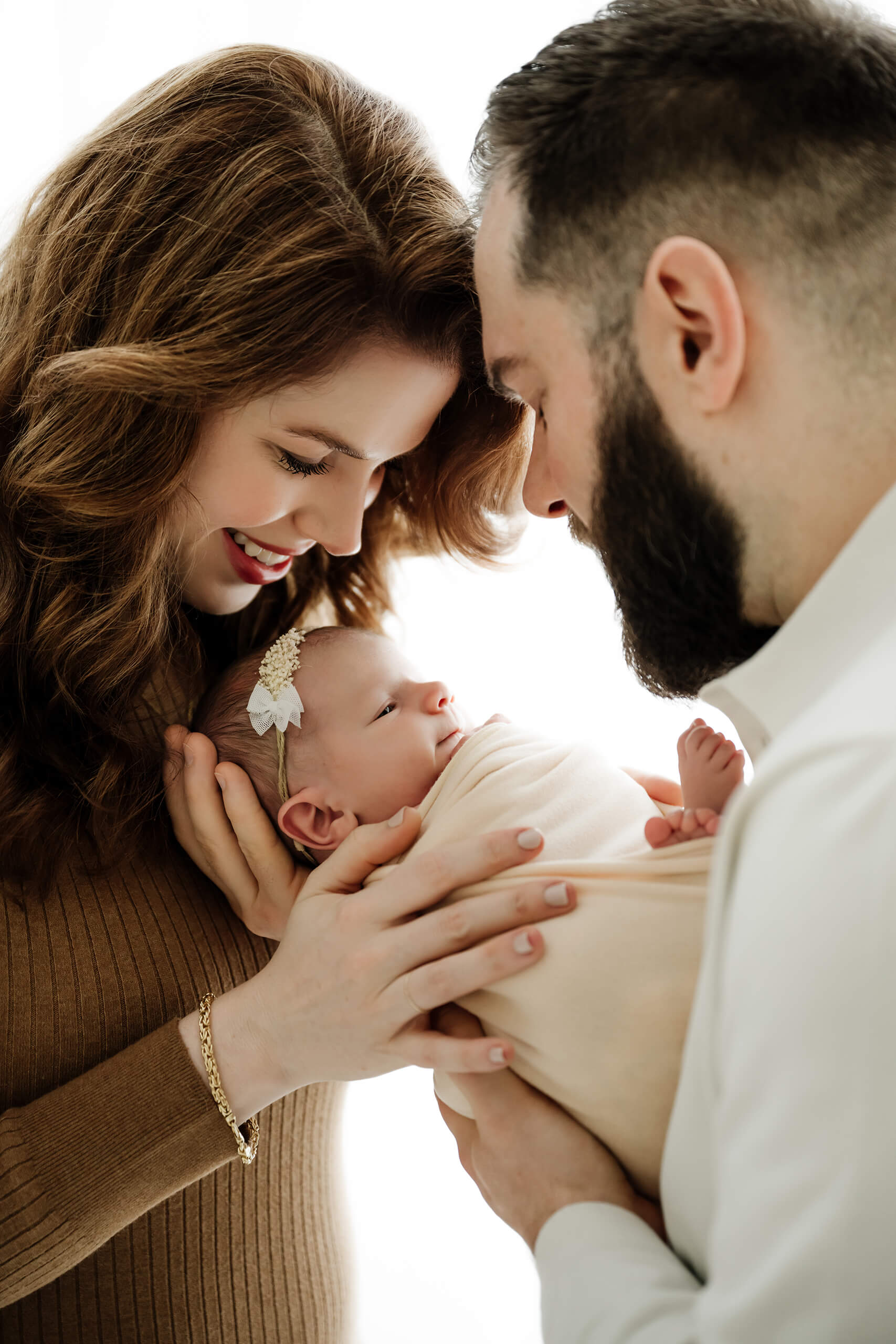 Parents cradle newborn between them by a window, close-up family connection portrait in a Seattle studio