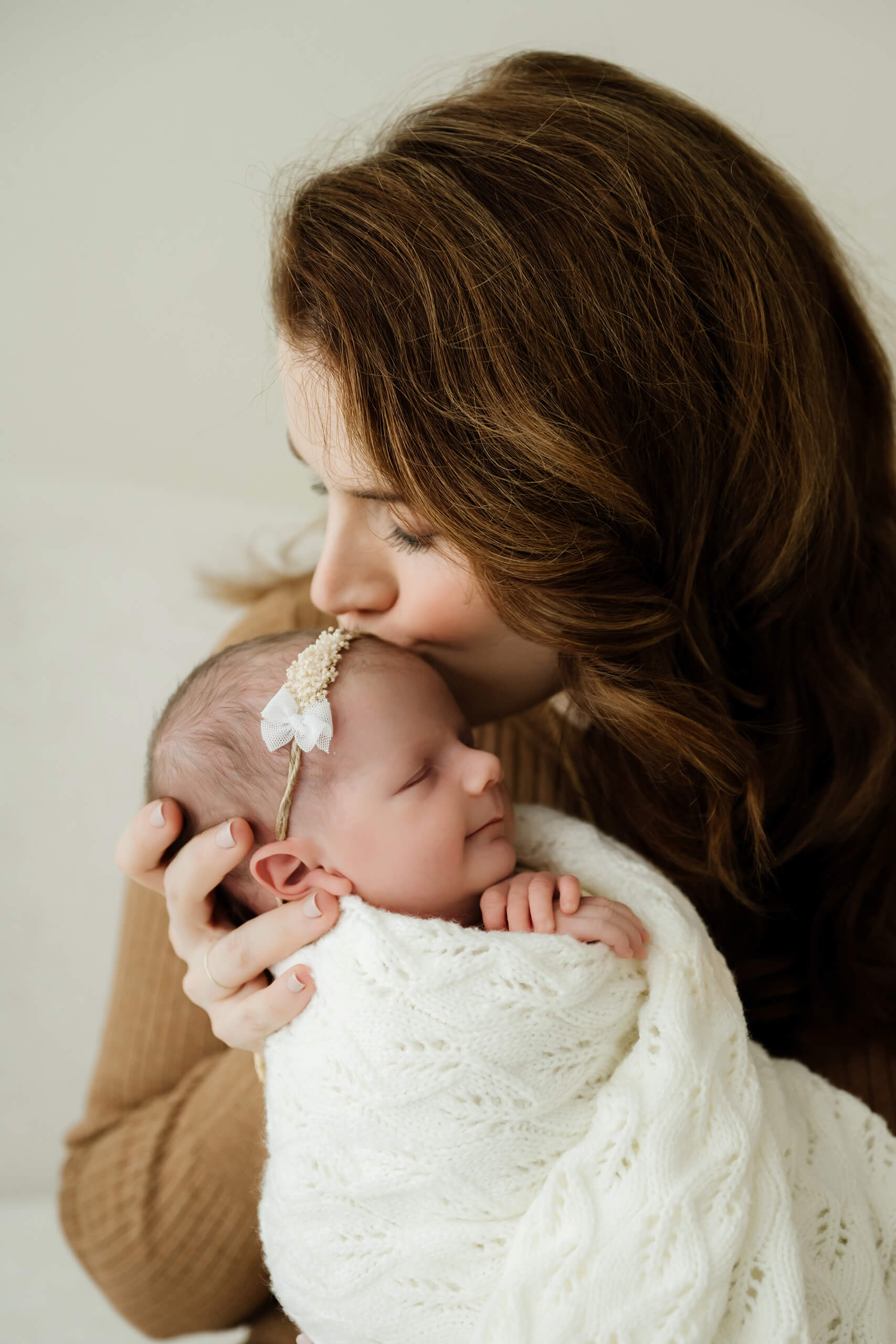 Mom kisses newborn’s head while baby rests wrapped in a knit blanket, tender close-up portrait in a Seattle studio