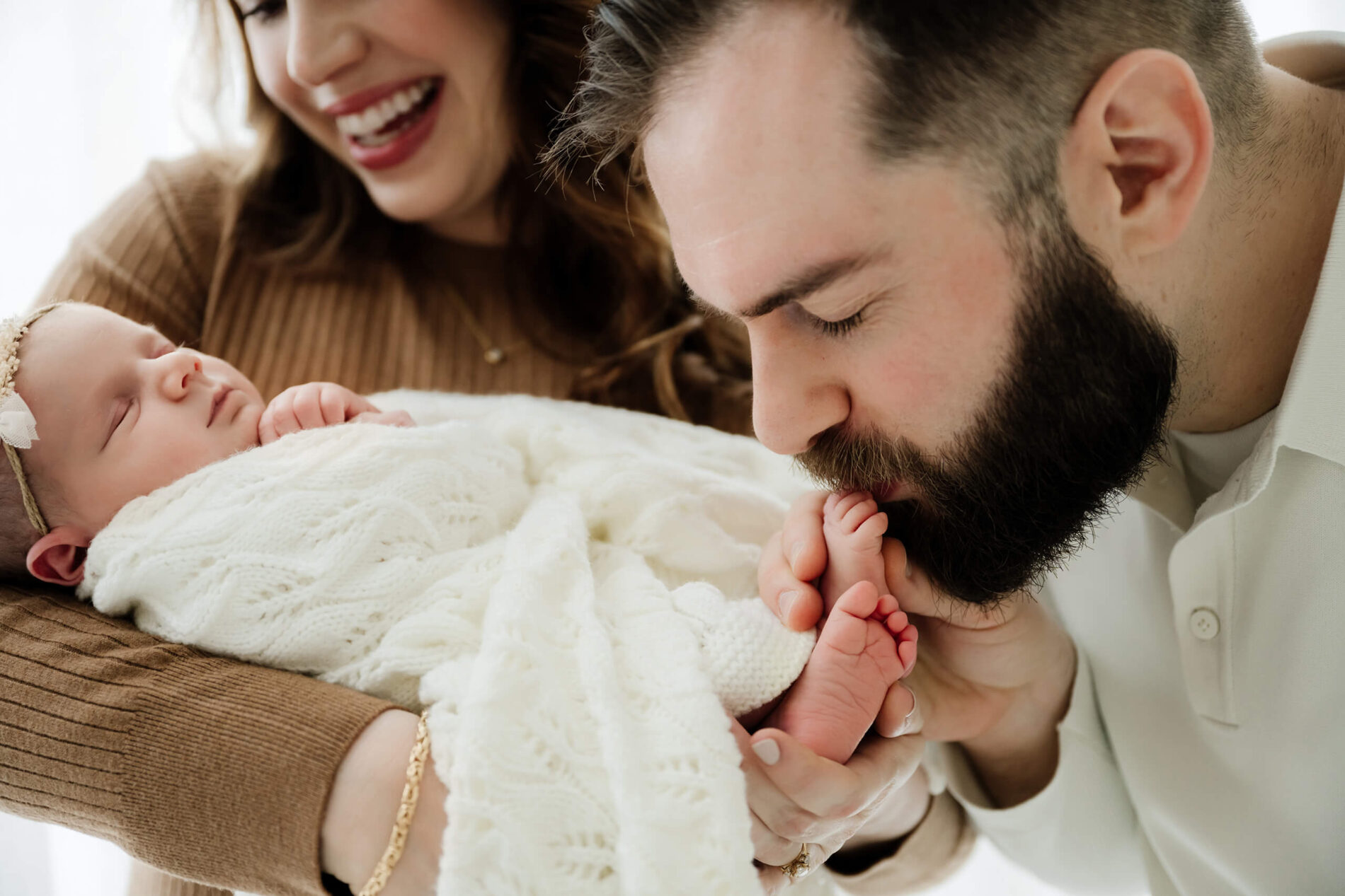 Dad kisses newborn’s toes while mom holds baby, playful family newborn moment during Seattle newborn family photoshoot