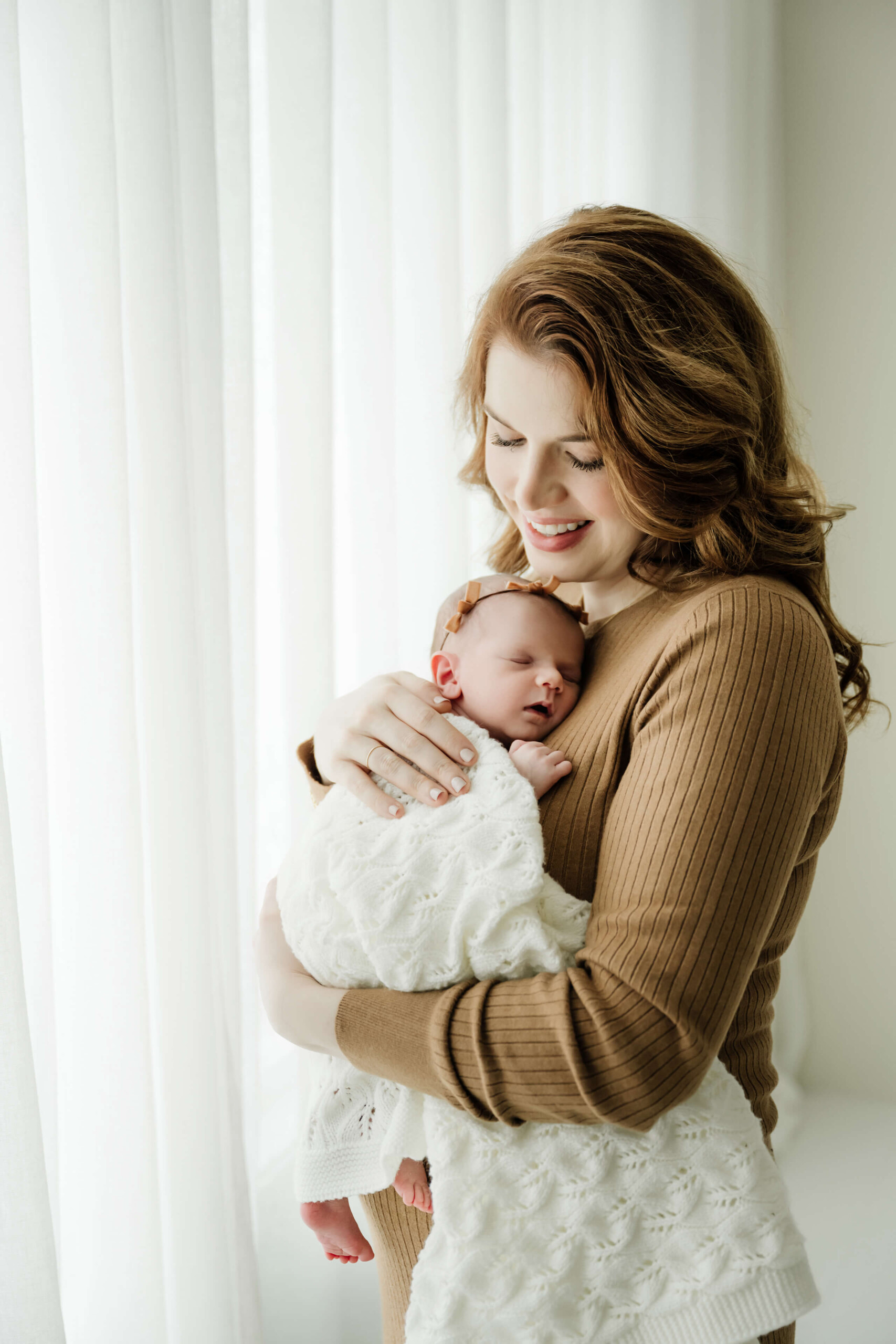 Seattle family newborn photoshoot with mom holding a swaddled newborn by the studio window