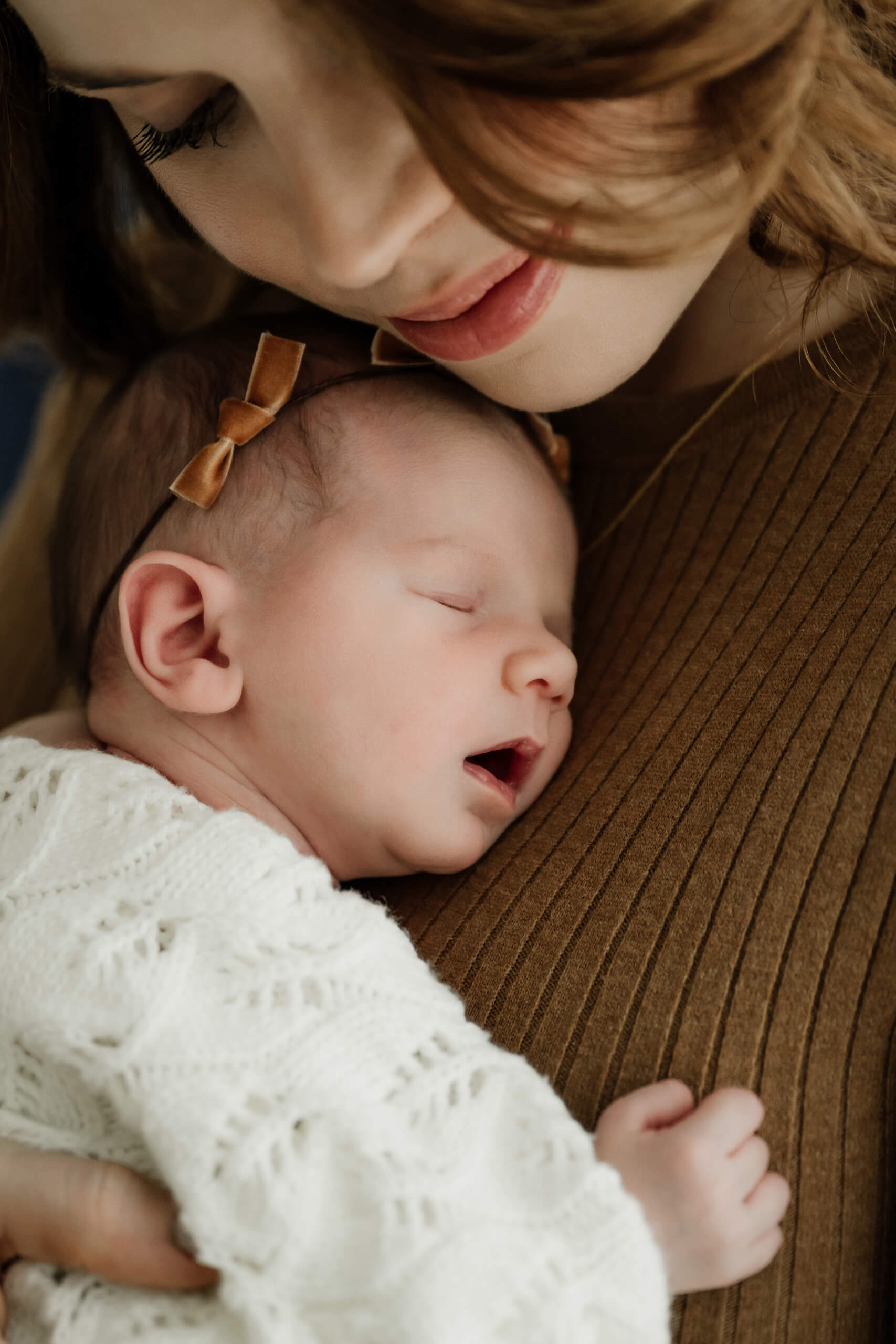 A close-up of mom cuddling a sleeping newborn with bow headband during a family newborn photography in Seattle