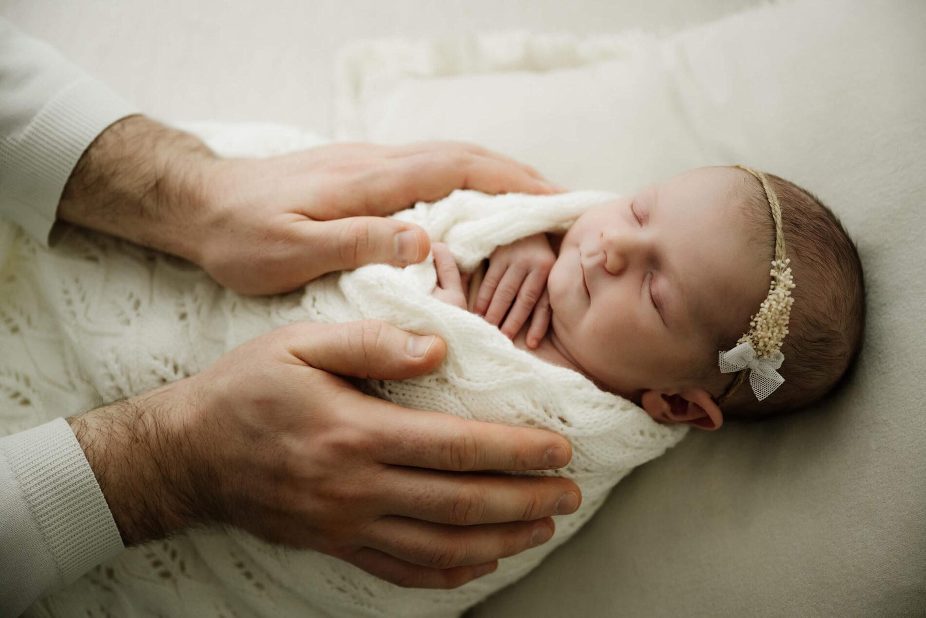 Parent hands gently support a swaddled newborn on the bed during a Seattle newborn family photoshoot