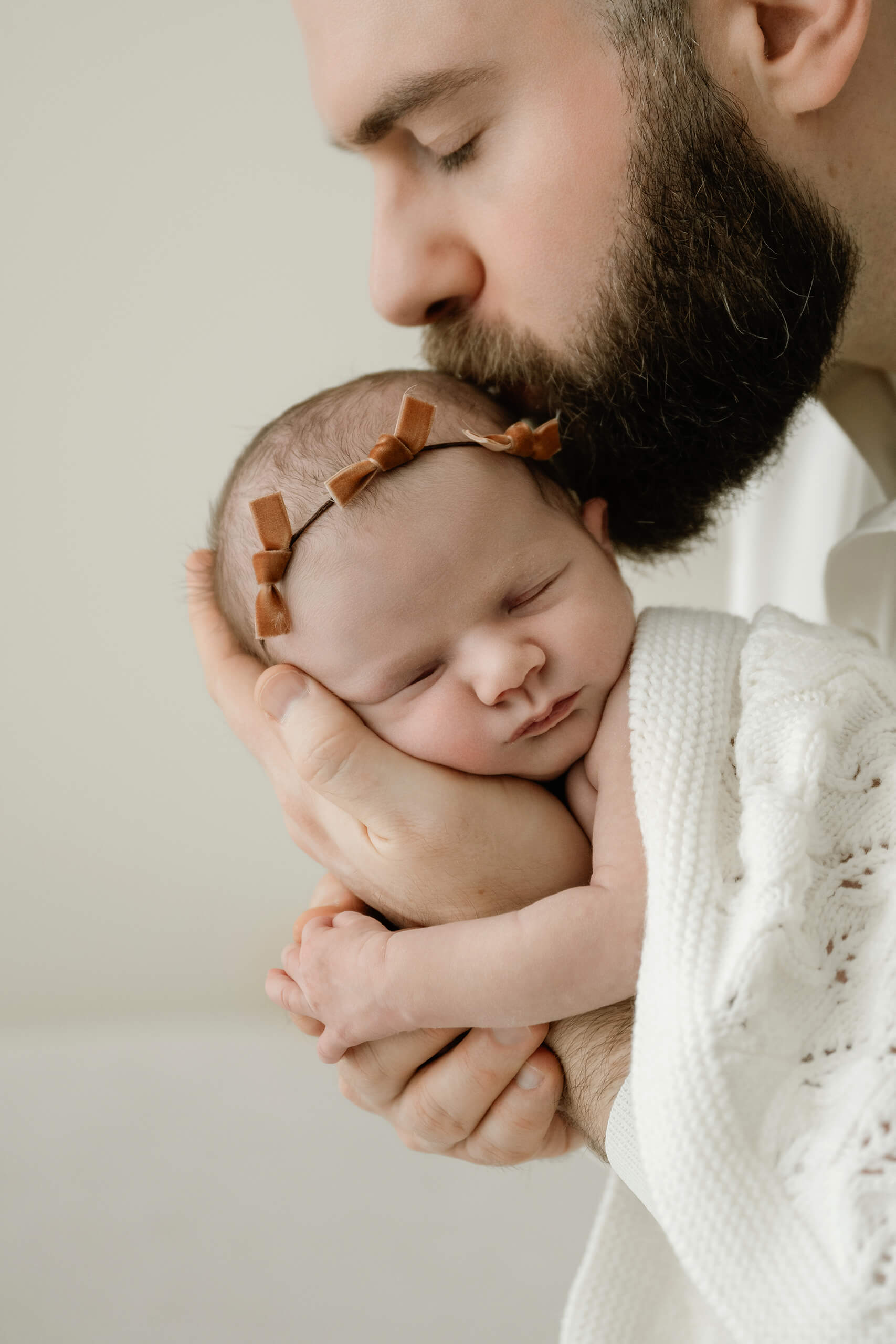 Dad kisses his sleeping newborn while holding her securely during a Seattle family newborn photoshoot