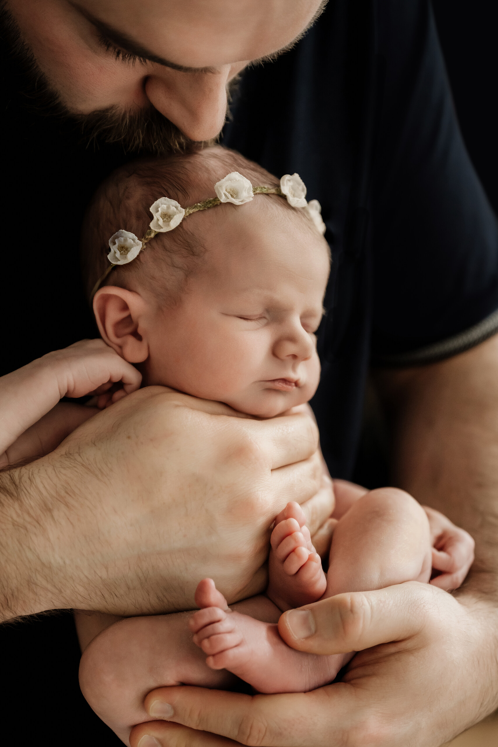 Dad kisses his newborn’s head while holding her safely during a Seattle newborn family photoshoot