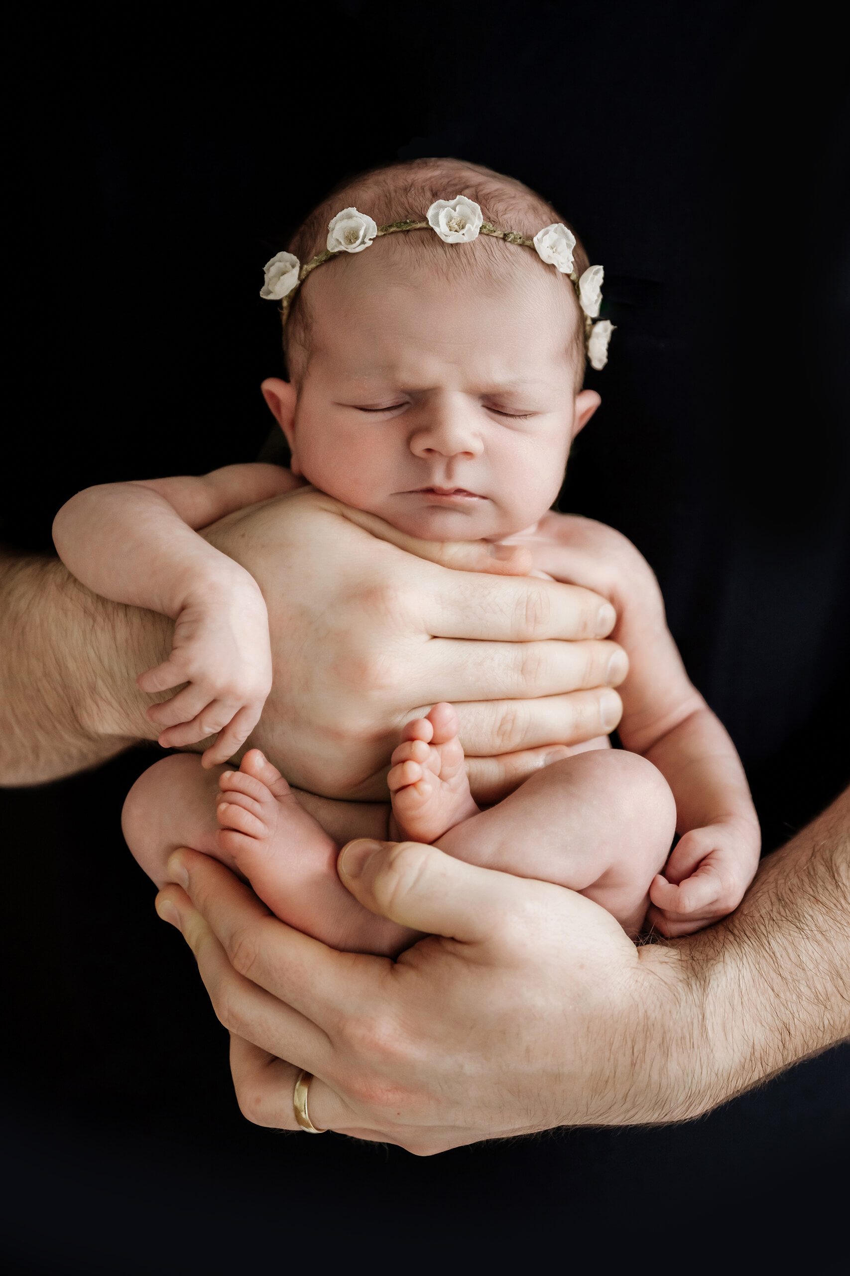 Newborn girl rests in dad’s hands with a delicate flower headband for family newborn photography in Seattle