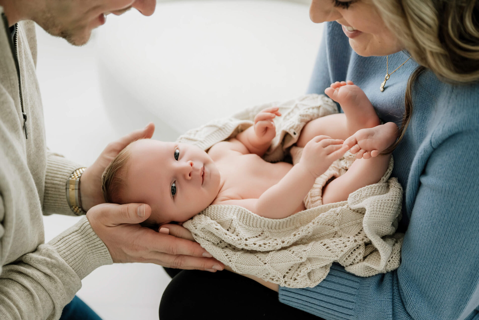 Parents hold their wide awake baby wrapped in a cozy knit blanket during a Seattle newborn family photoshoot
