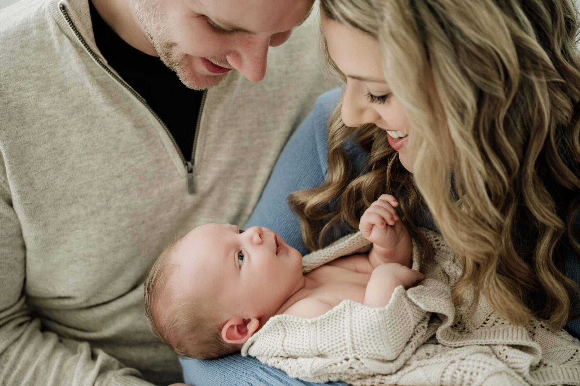 Mom and dad smile down at their baby during a Seattle family newborn photoshoot in the studio