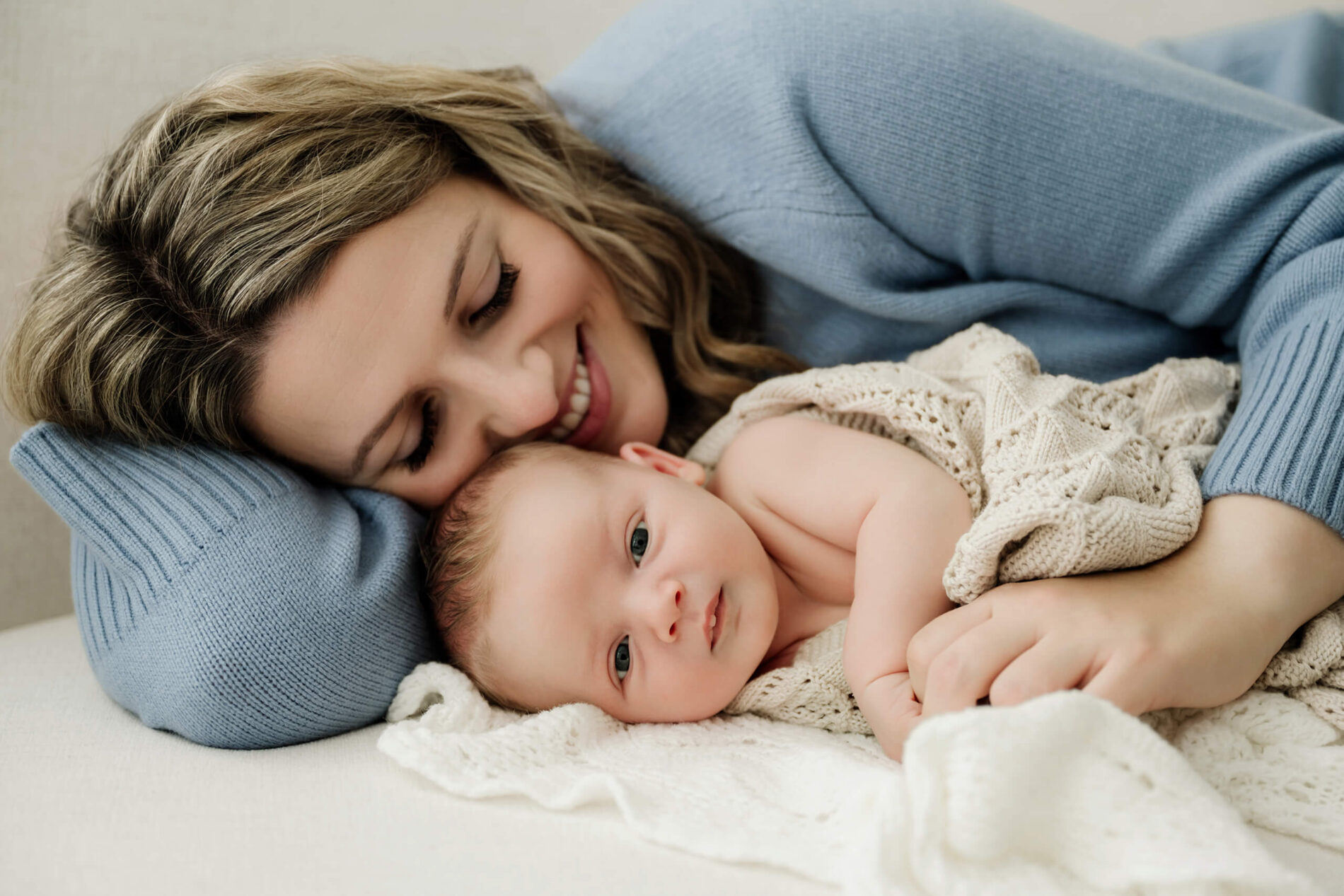 Mom snuggles close with her awake newborn on the bed for family newborn photography in Seattle
