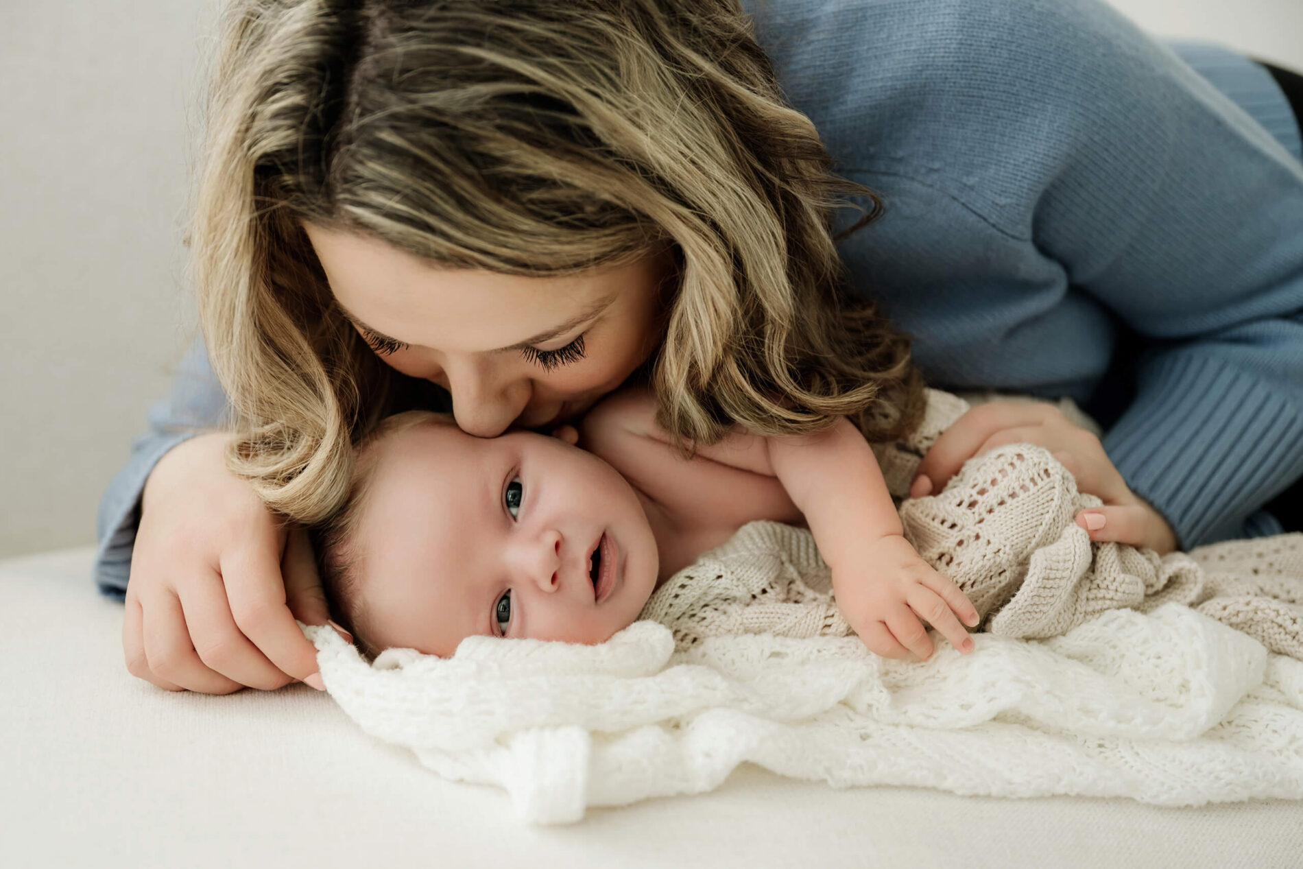 Mom kisses her baby’s head while cuddling together during a Seattle newborn family photoshoot