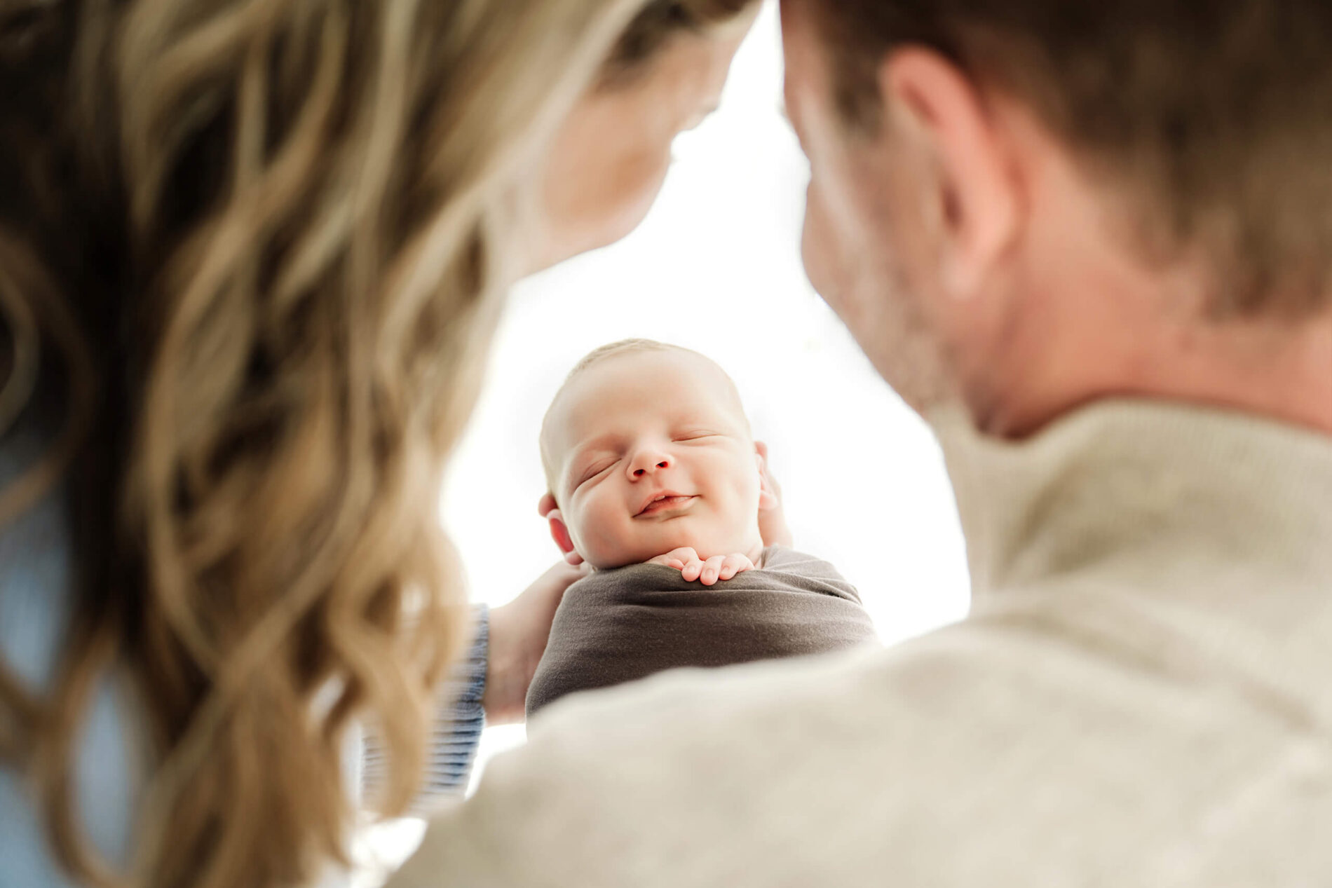 A swaddled newborn smiles softly while parents lean in close during a Seattle newborn family photoshoot