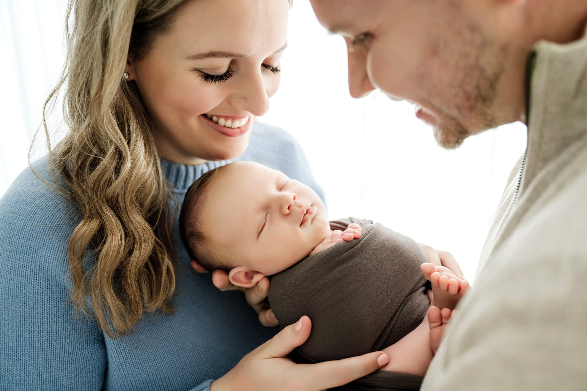 Mom holds her sleeping newborn while dad looks on during a Seattle family newborn photoshoot