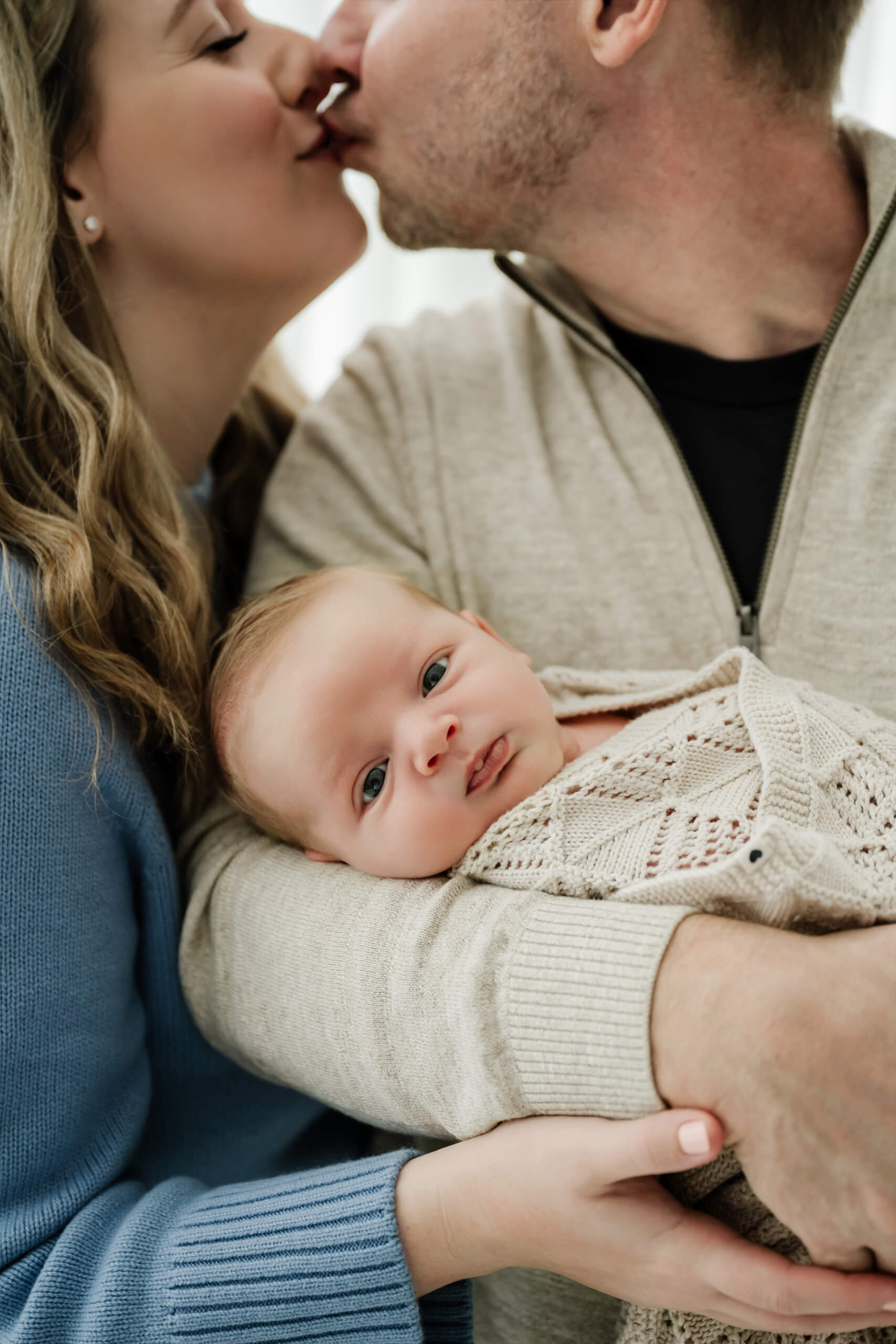 Parents share a kiss while holding their baby close in a Seattle family newborn photoshoot.