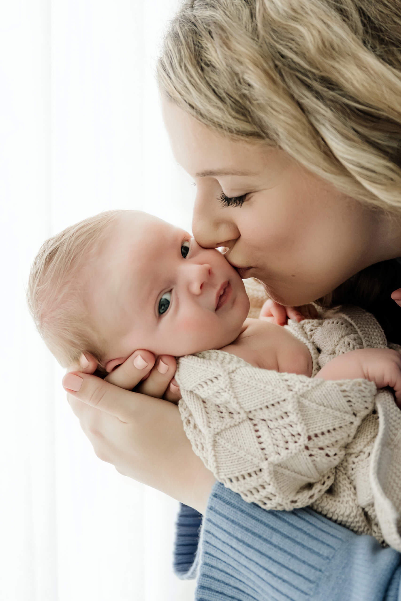 Mom kisses her baby’s cheek and the baby looks toward the camera in a Seattle newborn family photoshoot.