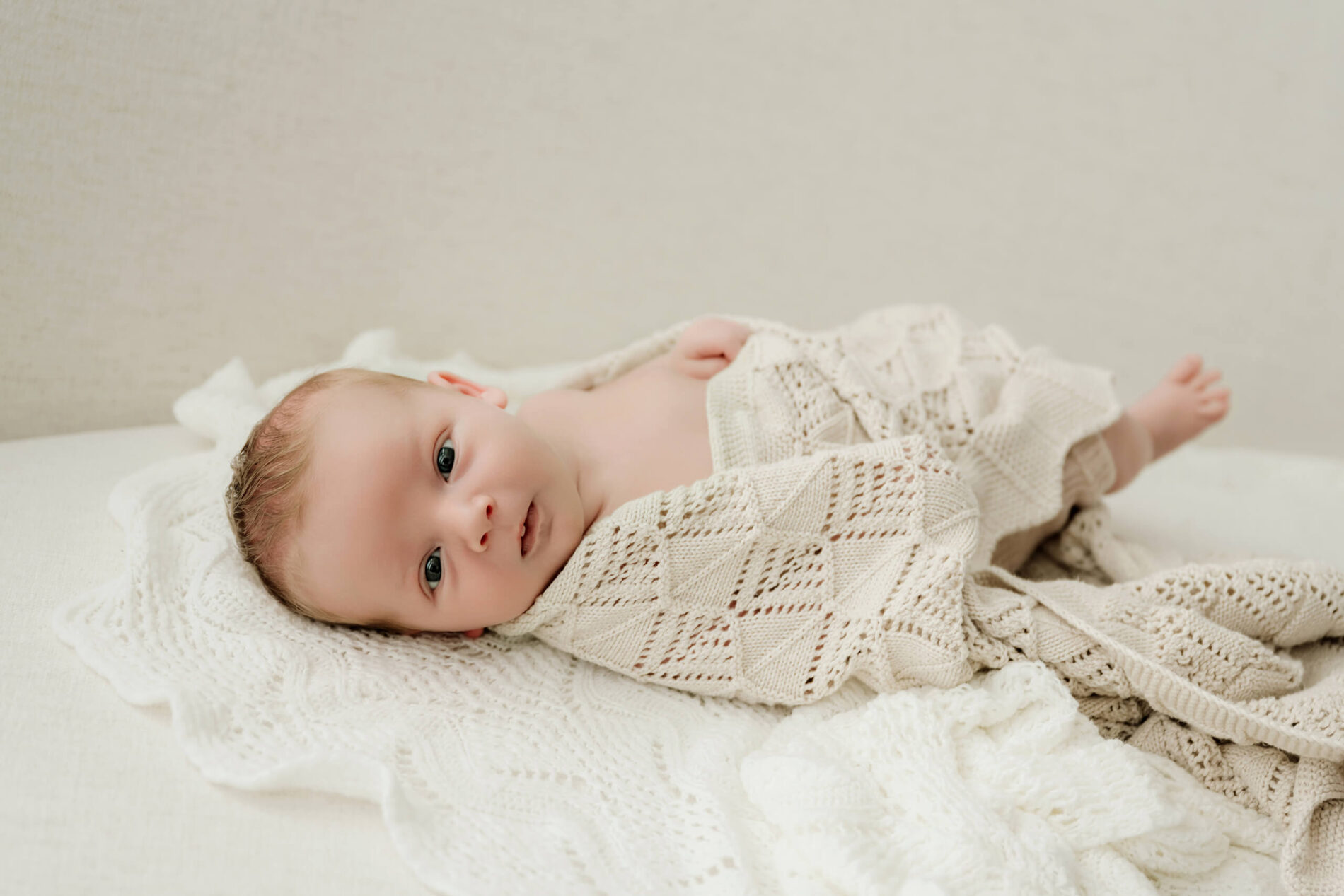 Baby lying on a white blanket with a knitted wrap, captured during Seattle newborn family photography.