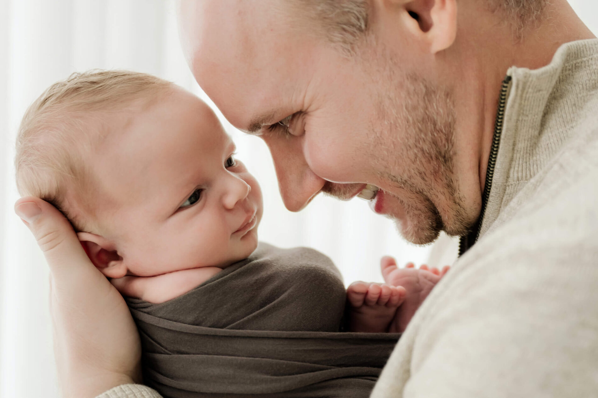 Dad holds his swaddled newborn close and smiles at them during a Seattle family newborn photoshoot.