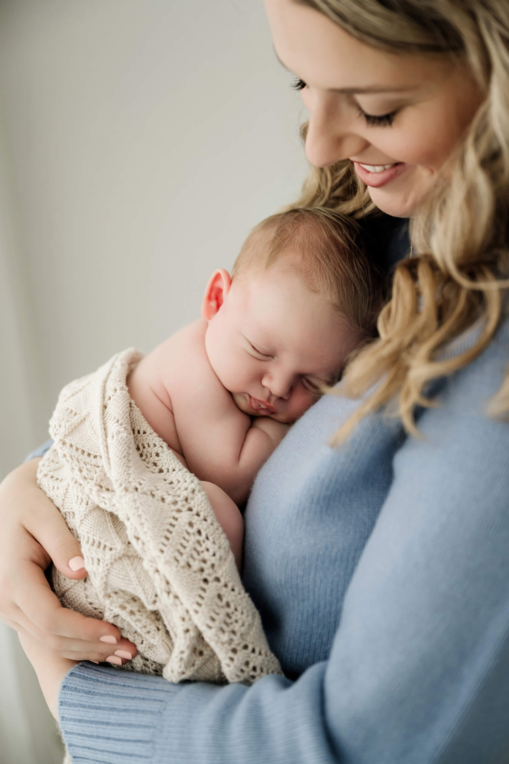 Newborn family photography in Seattle showing mom holding sleeping baby on her shoulder with a knit blanket wrap.