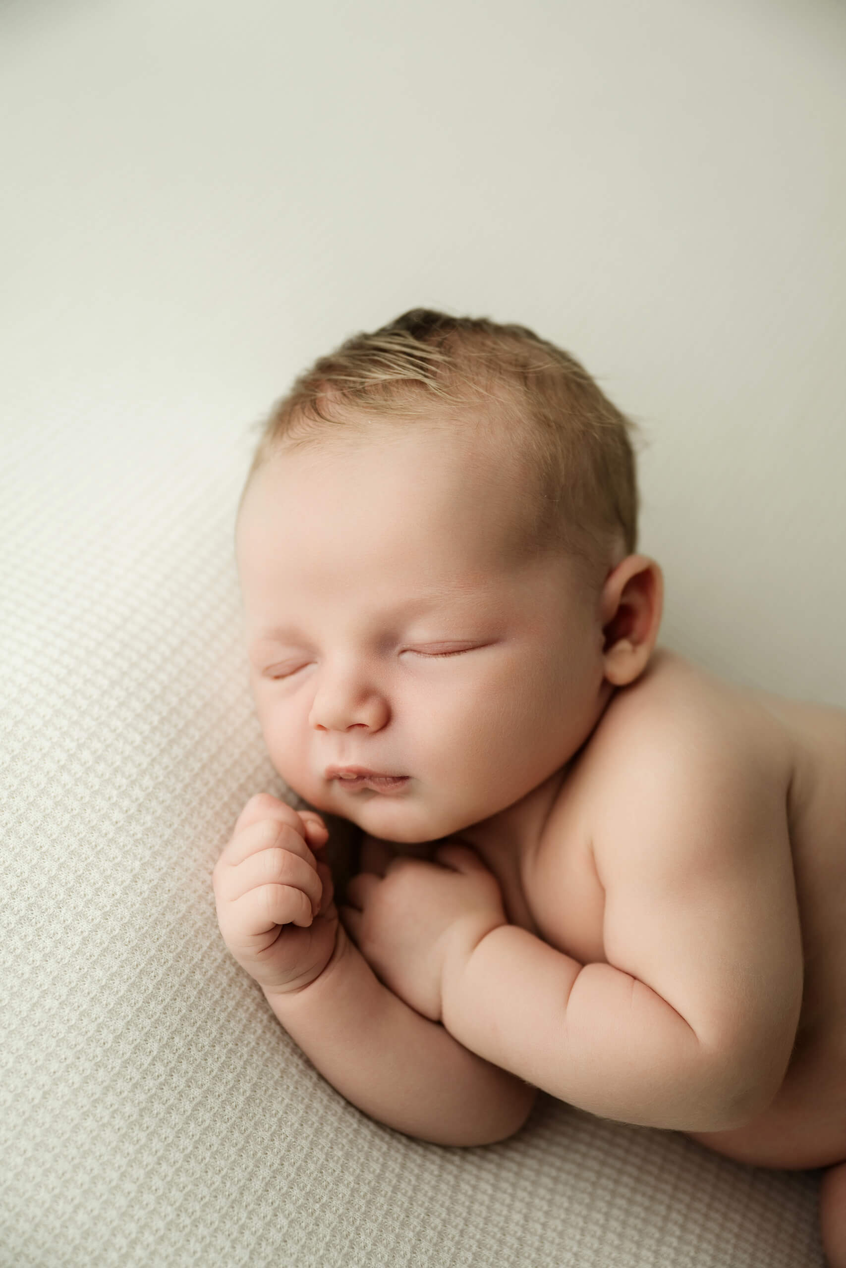 Seattle newborn photoshoot of sleeping baby posed on a white textured blanket, soft side-lying pose.