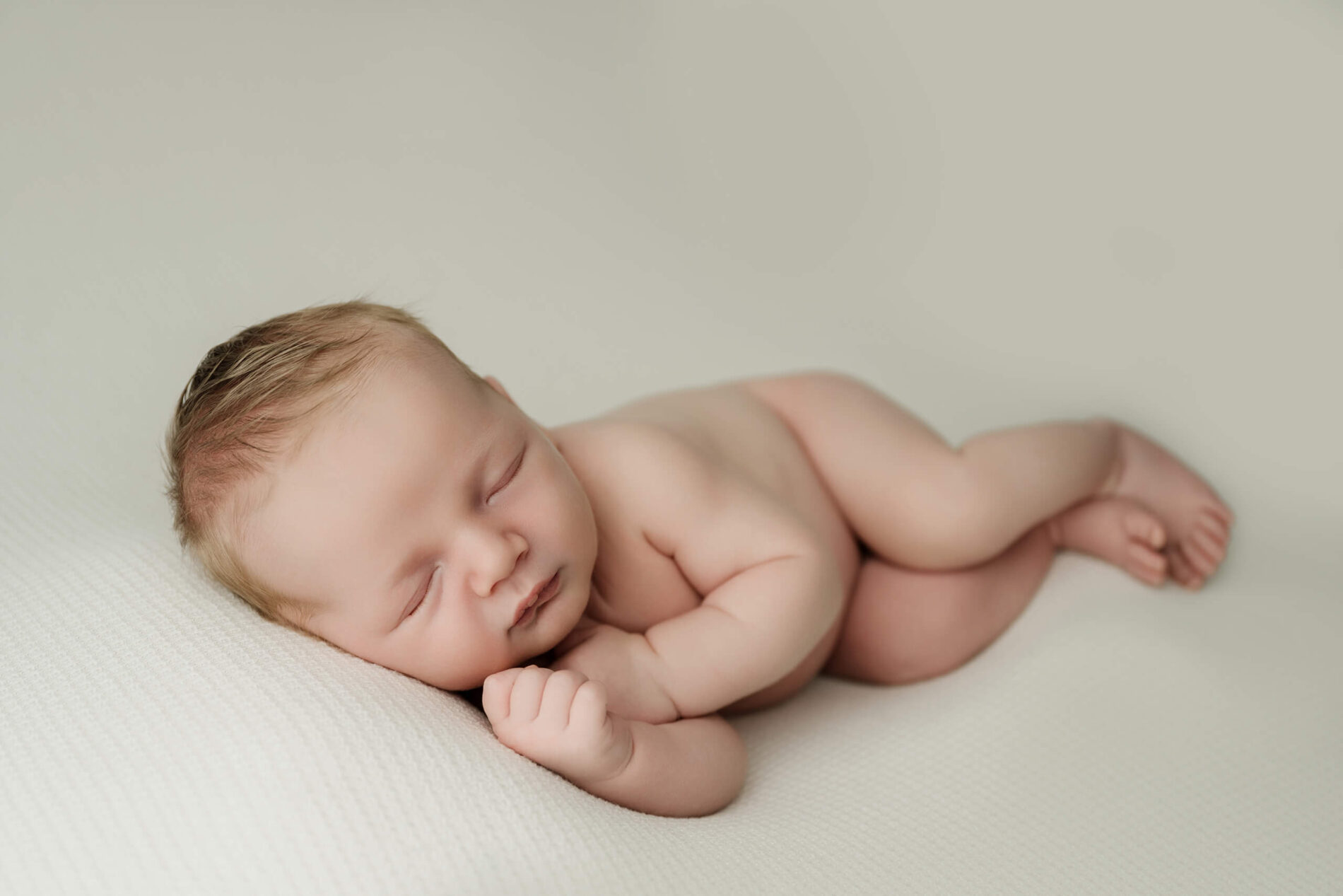 Seattle newborn photoshoot of baby sleeping curled on a white textured blanket, minimal studio backdrop.