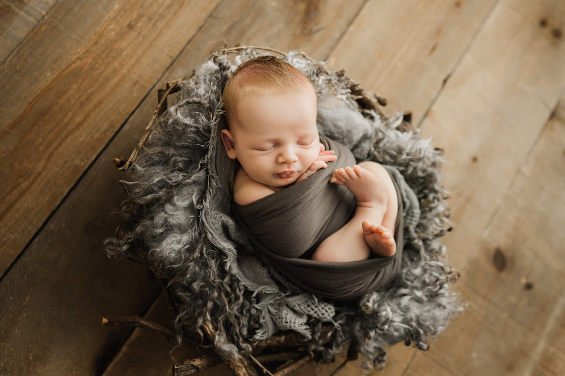 Seattle newborn photoshoot of wrapped baby sleeping in a gray nest on wooden floor, overhead view.