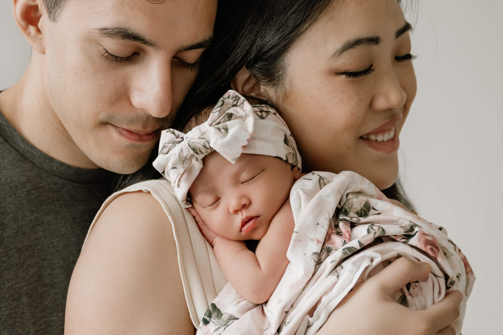 Sleeping newborn wrapped in a floral swaddle, held closely by parents during a Seattle Newborn In-Home Lifestyle Session
