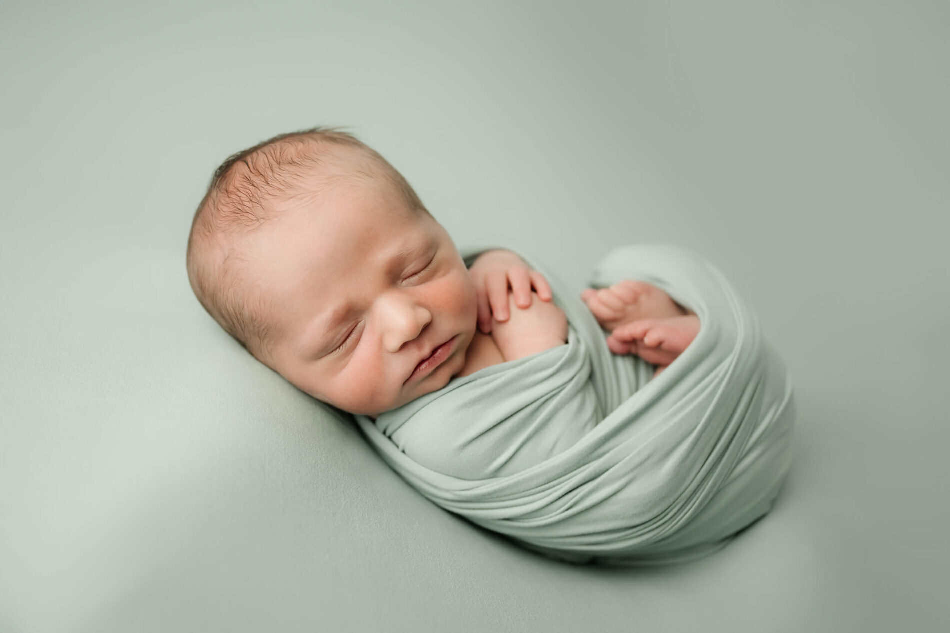 Sleeping newborn wrapped in soft sage fabric, photographed on a neutral studio backdrop during a mini newborn session in Seattle.