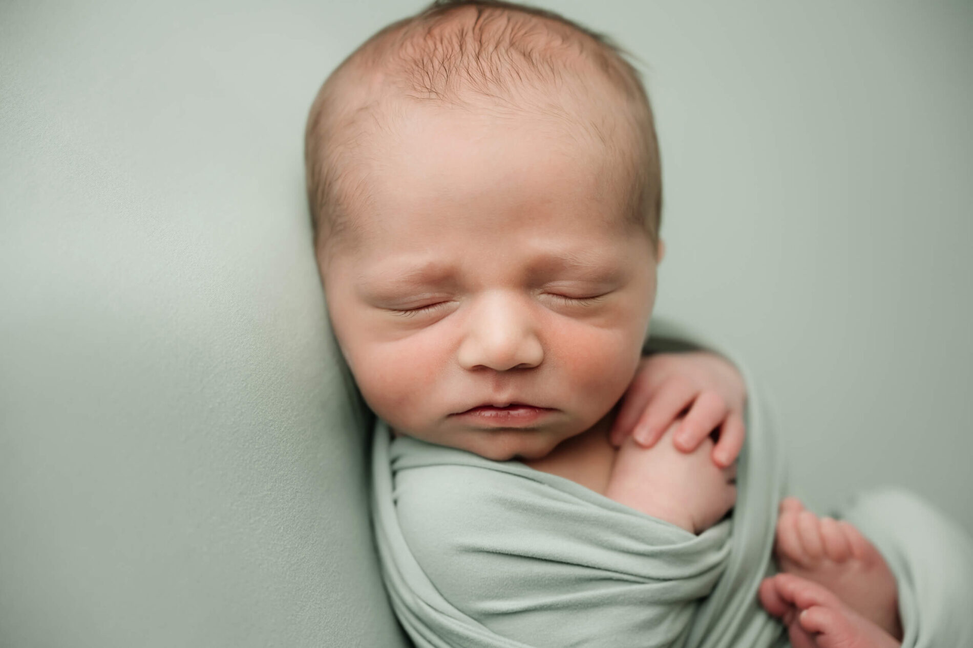 Close-up portrait of a wrapped newborn with relaxed hands and peaceful expression during a baby-focused studio newborn session in Seattle.