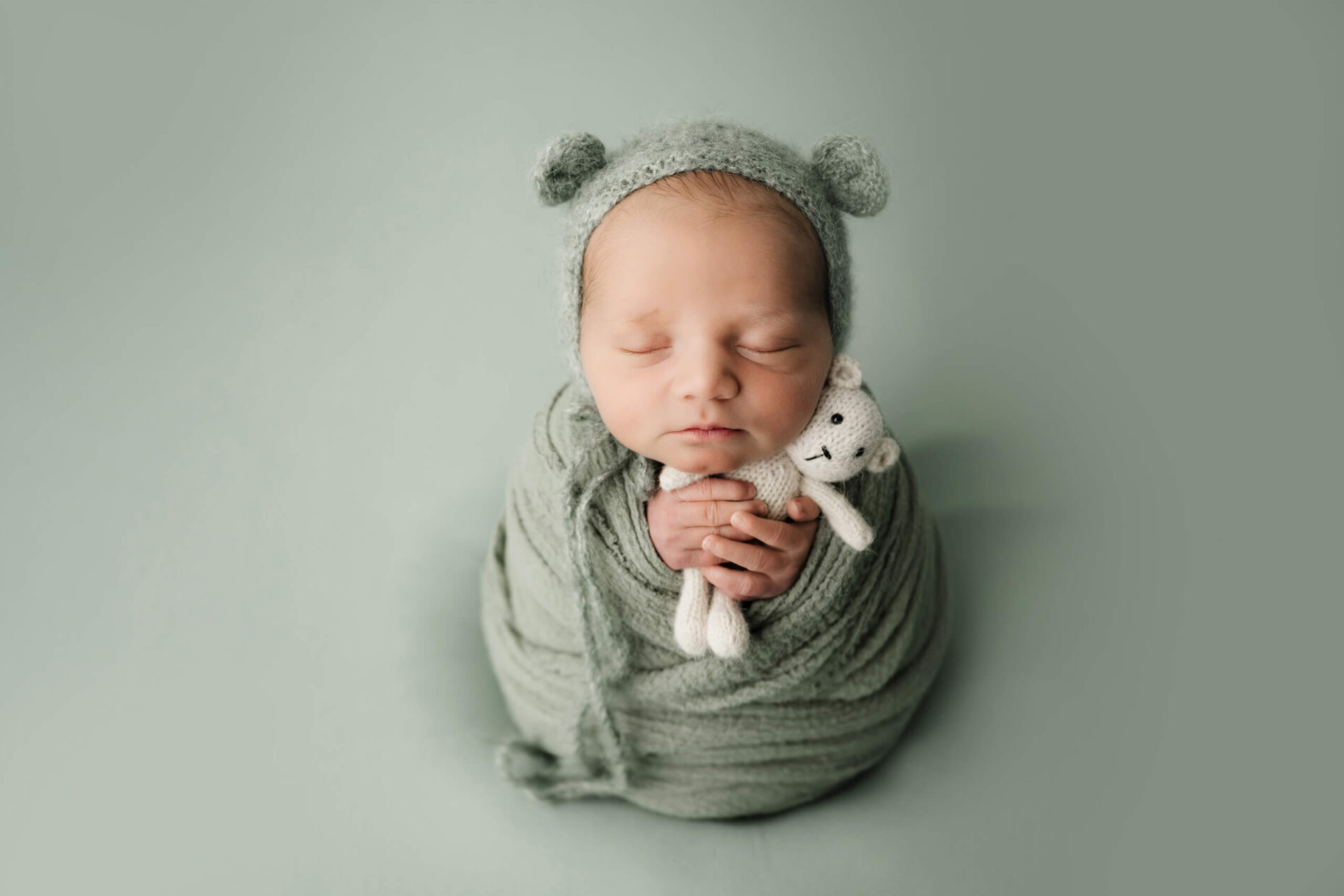 Wrapped newborn wearing a soft knit bonnet and holding a small stuffed toy, captured in a simple mini studio newborn session in Seattle.
