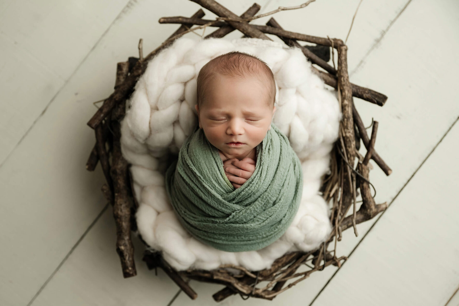 Top-down view of a wrapped newborn nestled in a rustic nest setup, captured during a minimalist mini studio newborn session in Seattle.
