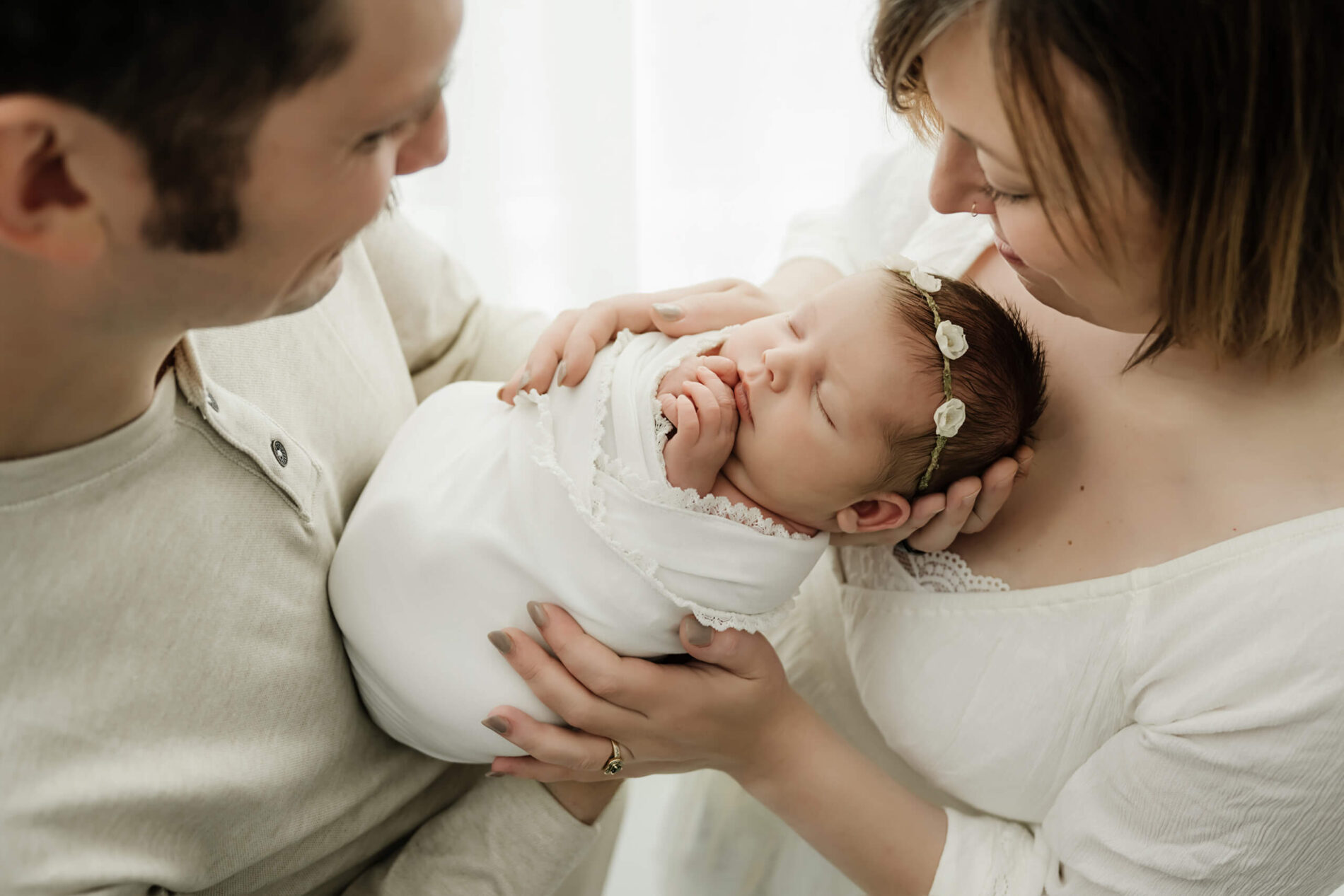 Parents holding their wrapped newborn together in a light-filled studio, captured during a simple family newborn session in Seattle.