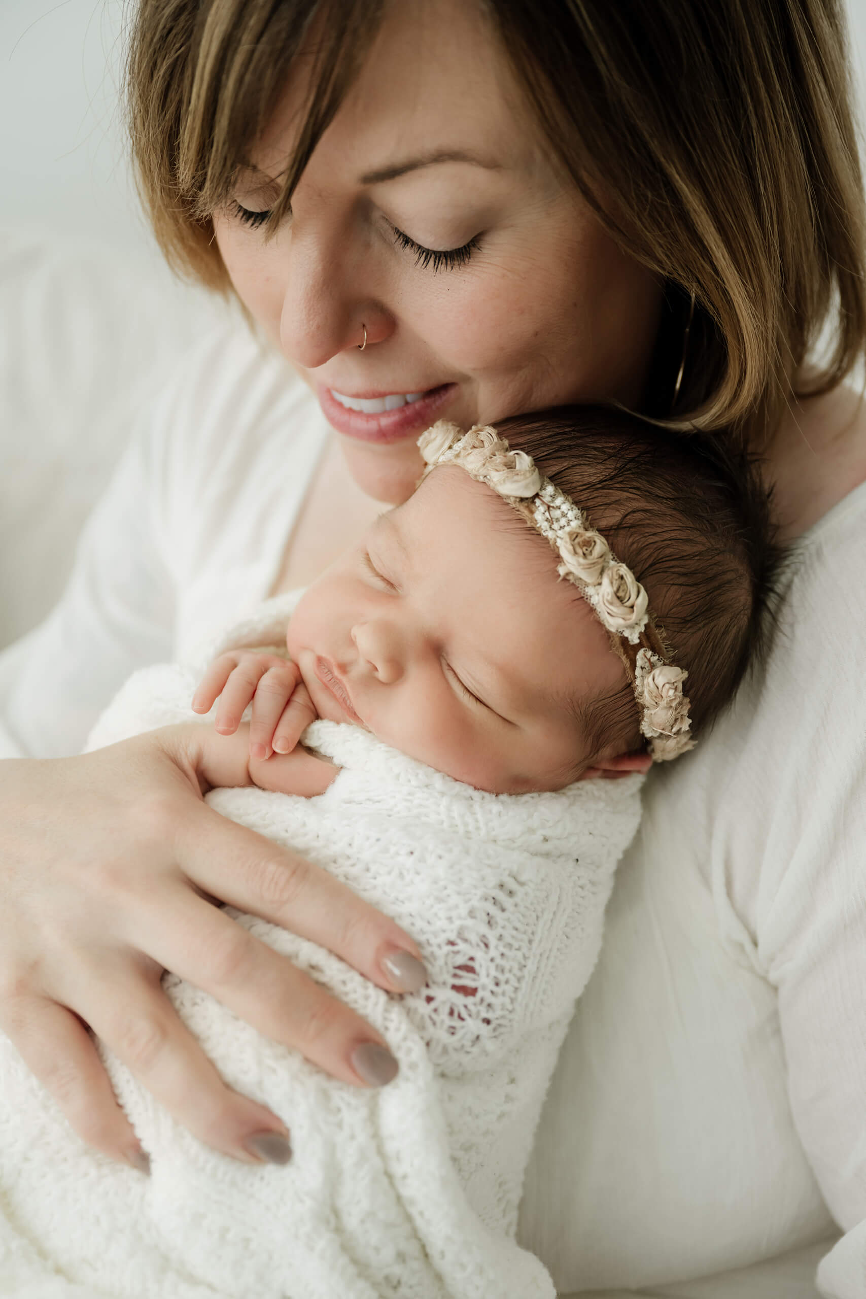 Mother holding her sleeping newborn wrapped in white, photographed during a gentle studio newborn session in Seattle.