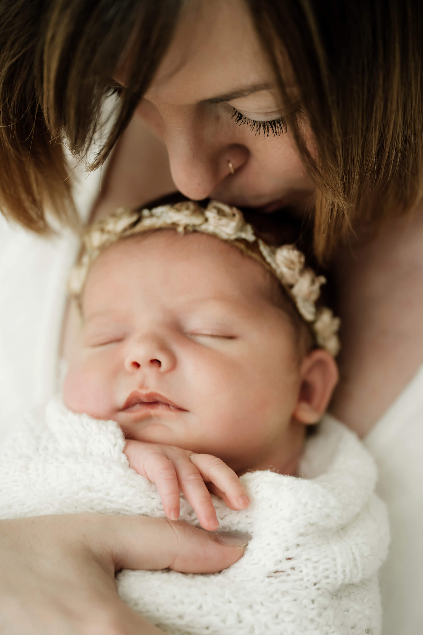 Close-up of a mother kissing her sleeping newborn wrapped in soft white fabric during an intimate studio newborn session in Seattle.