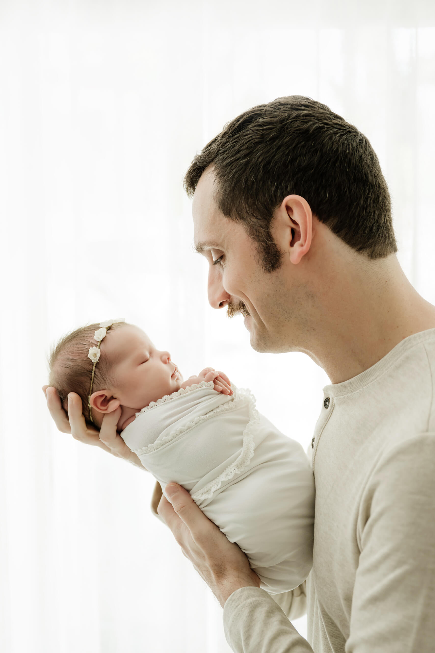 Father holding his wrapped newborn near a bright window, captured during a minimalist studio newborn session in Seattle.